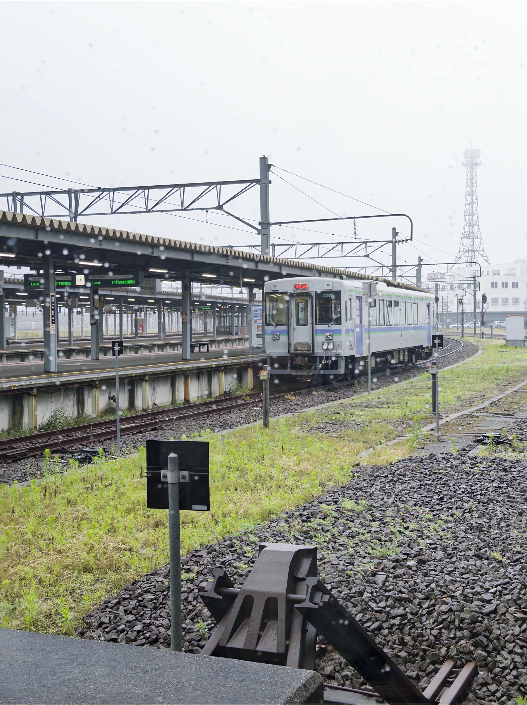 An early local train curving through rainy Hakodate Station at 5:36 in the morning