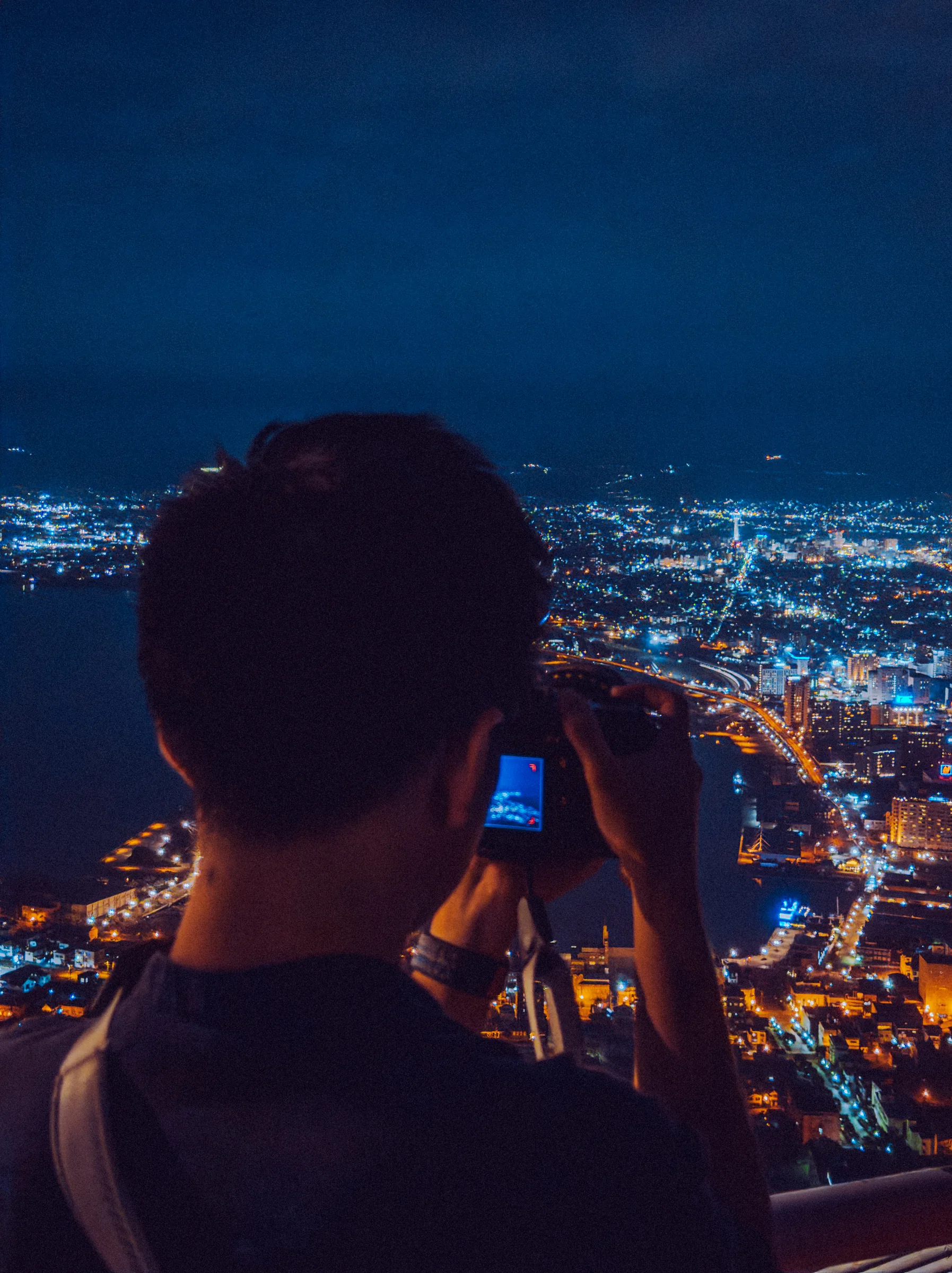A photographer silhouetted against Hakodate's night lights from Mount Hakodate