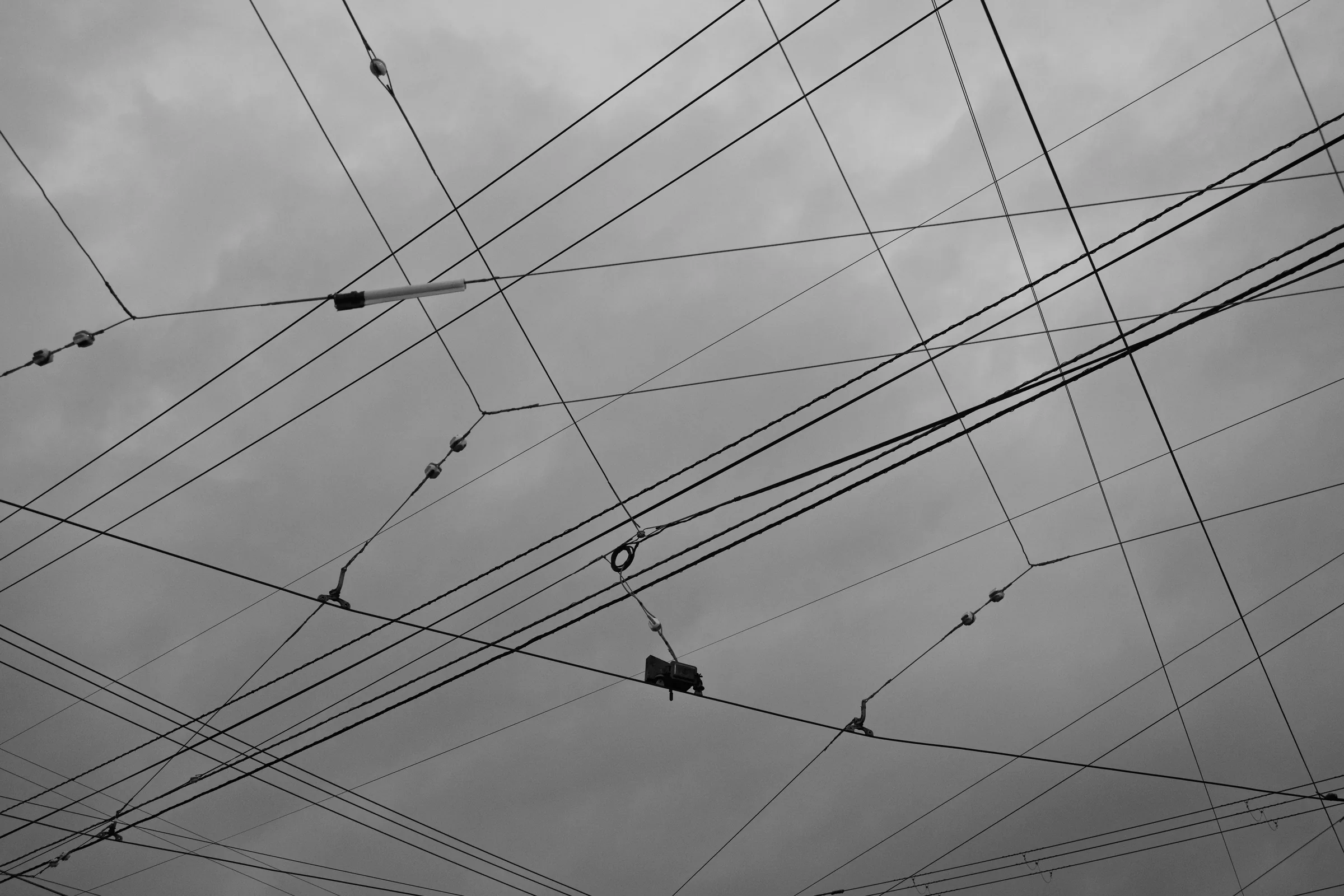 A web of tram and utility wires crossing a grey sky in black and white