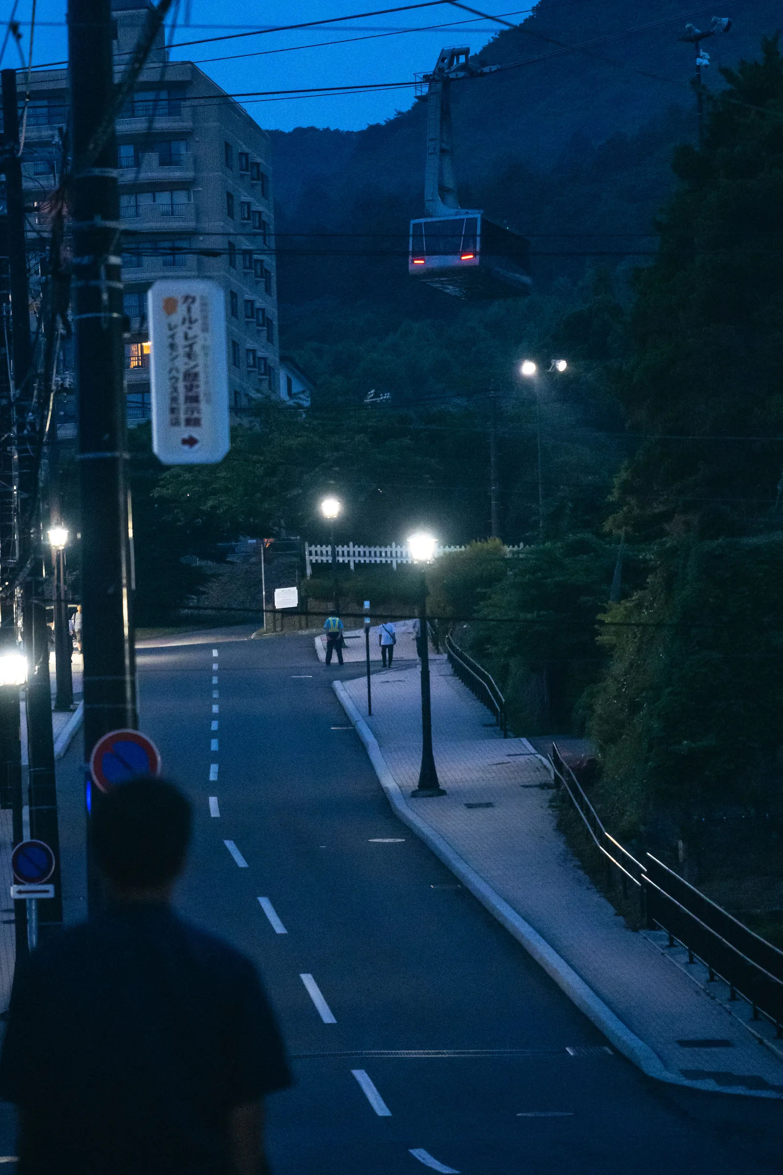 A Mount Hakodate Ropeway gondola suspended above a quiet road at dusk