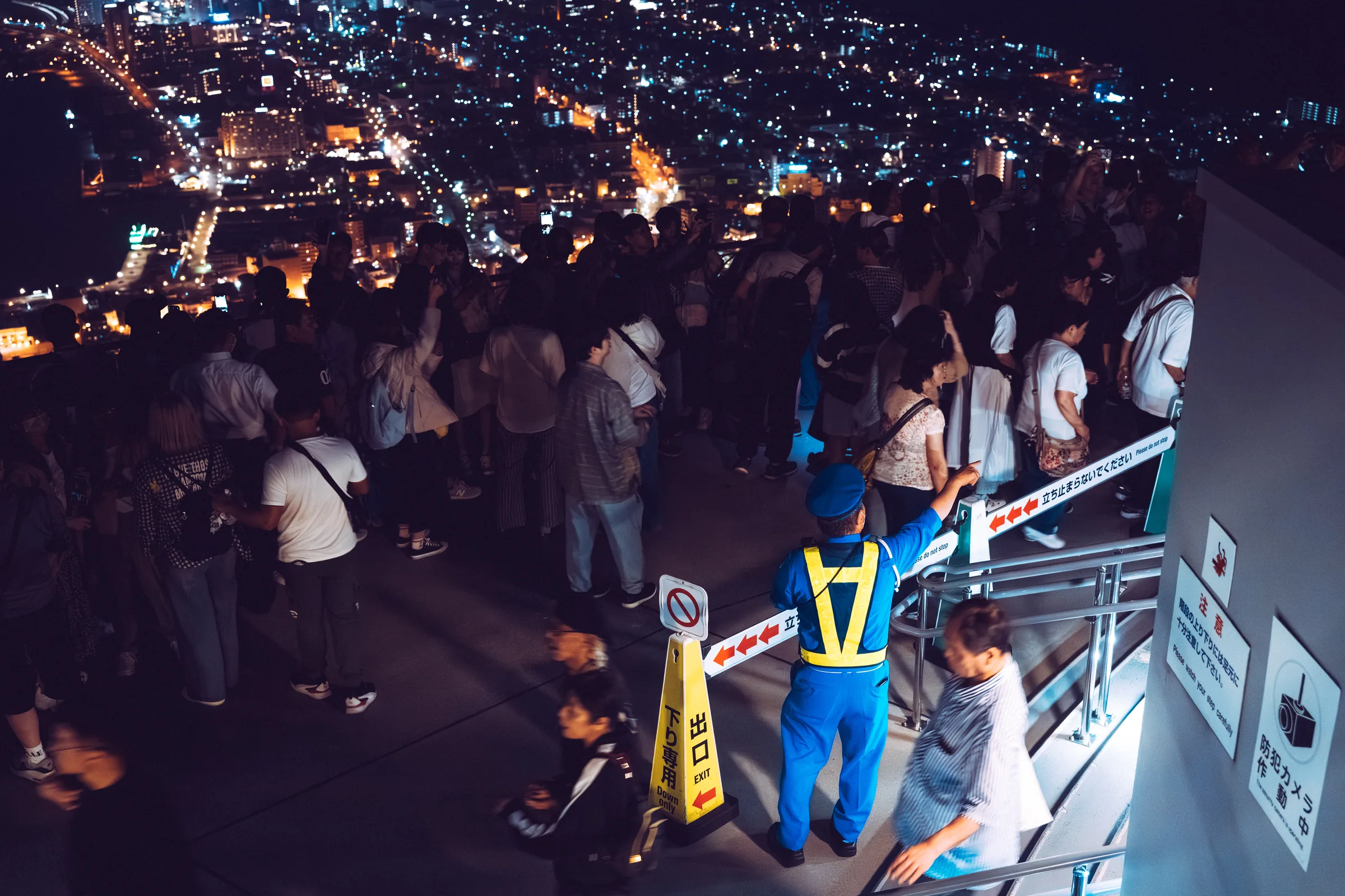 A uniformed attendant directing a dense crowd on the Mount Hakodate observation deck