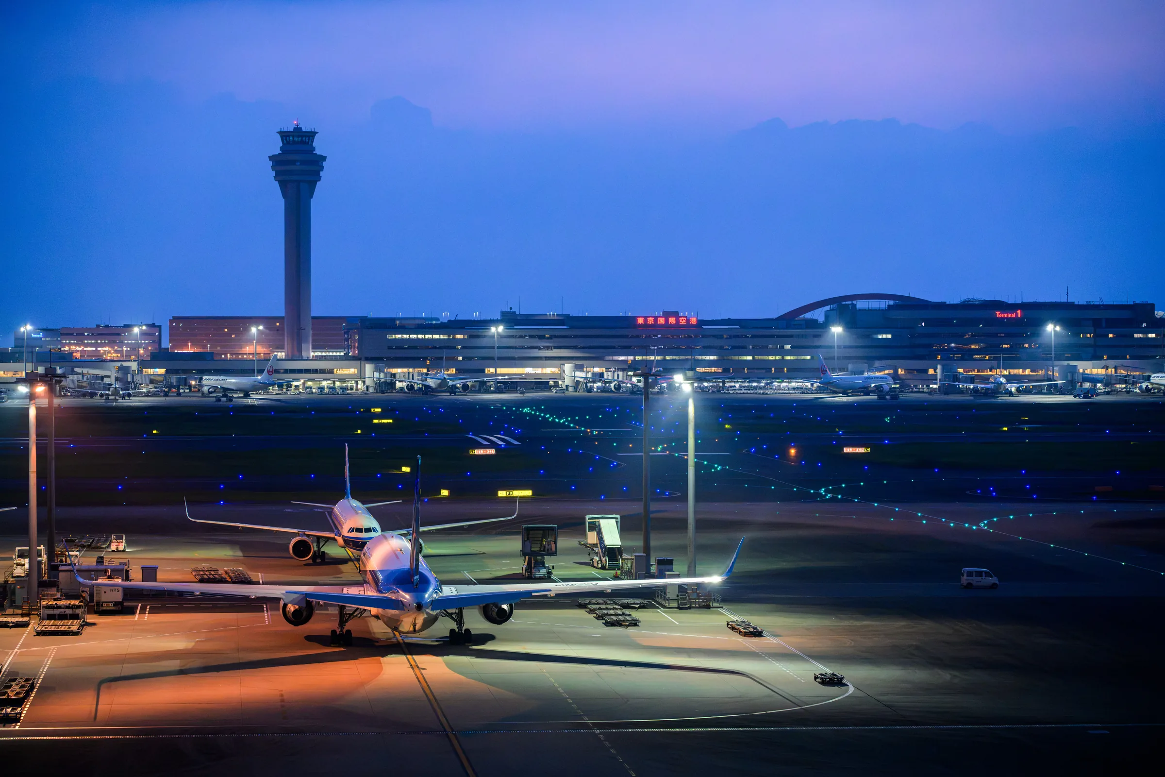 Haneda Airport glowing blue before sunrise with aircraft parked beneath the control tower