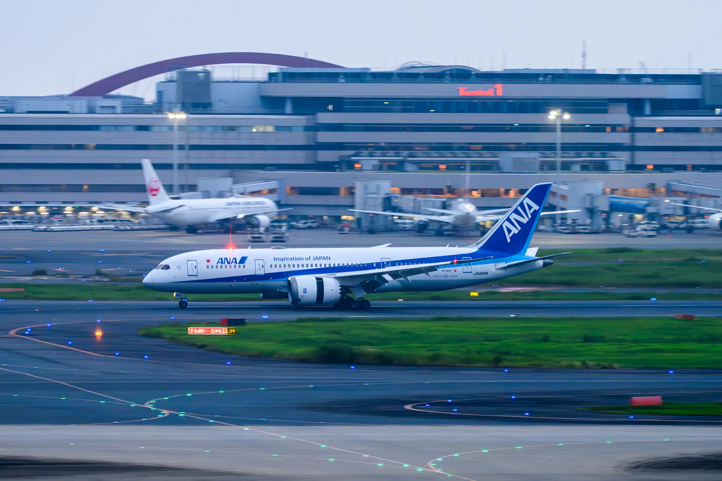 An ANA aircraft moving across green runway margins in a panning photograph
