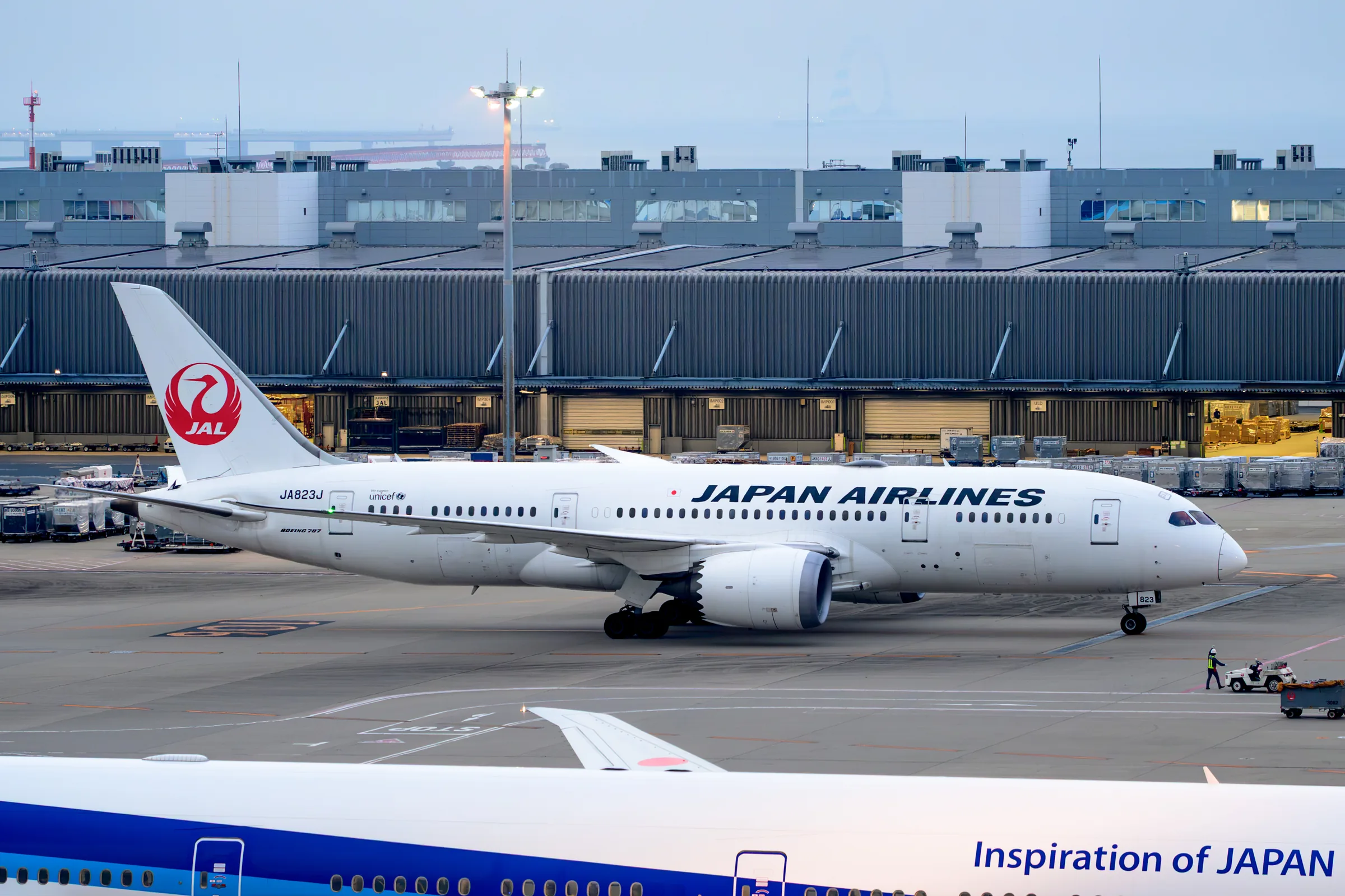A Japan Airlines aircraft taxiing across the airport in early daylight