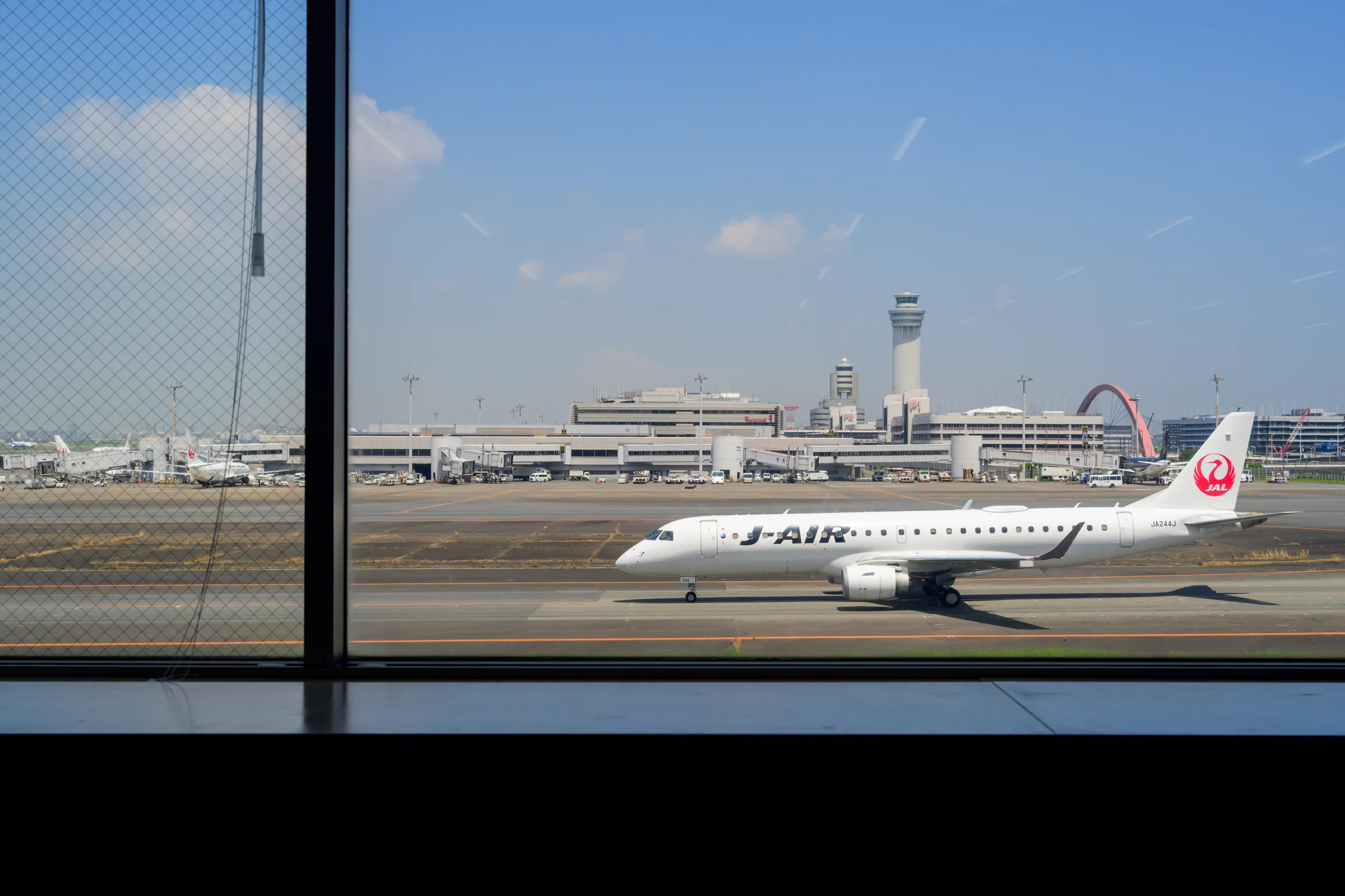 A J-Air aircraft crossing a window-framed view of Haneda Airport