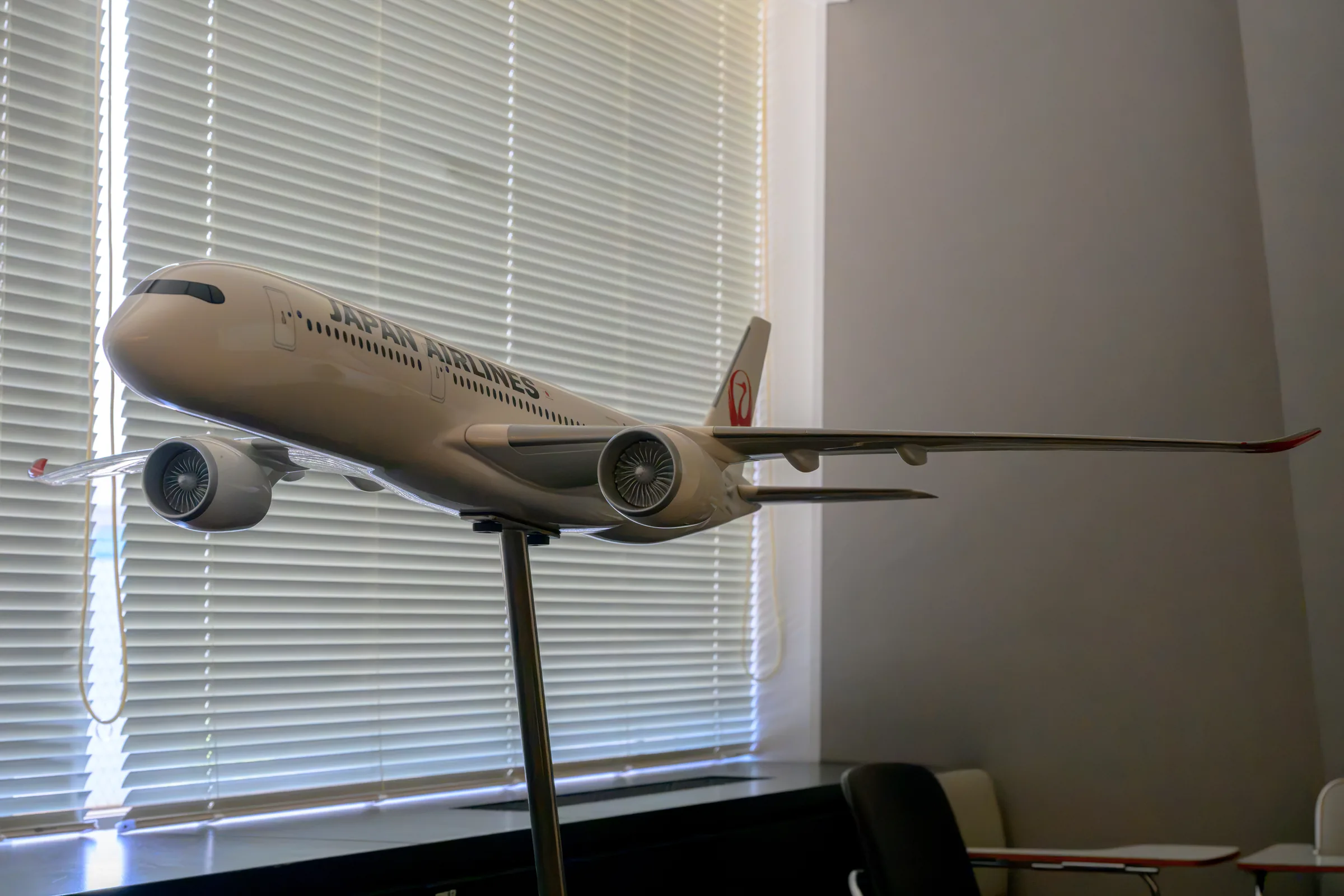 A Japan Airlines scale aircraft model lit beside museum window blinds
