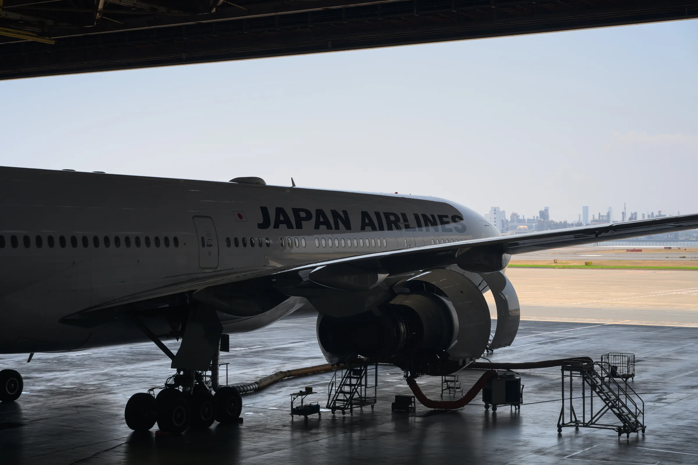 A Japan Airlines widebody aircraft silhouetted at the open edge of a hangar