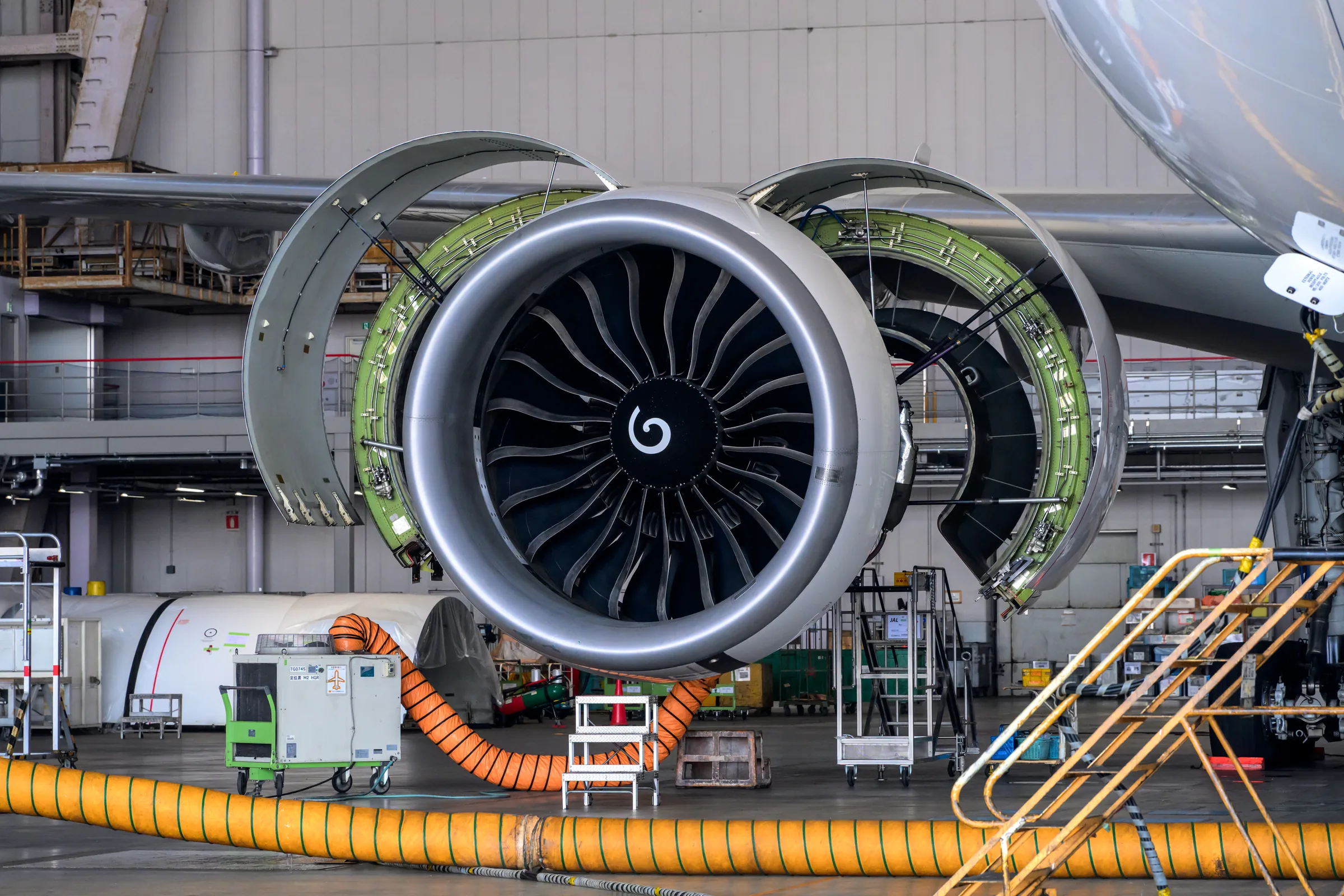 A large turbofan engine with its cowling opened inside a maintenance hangar