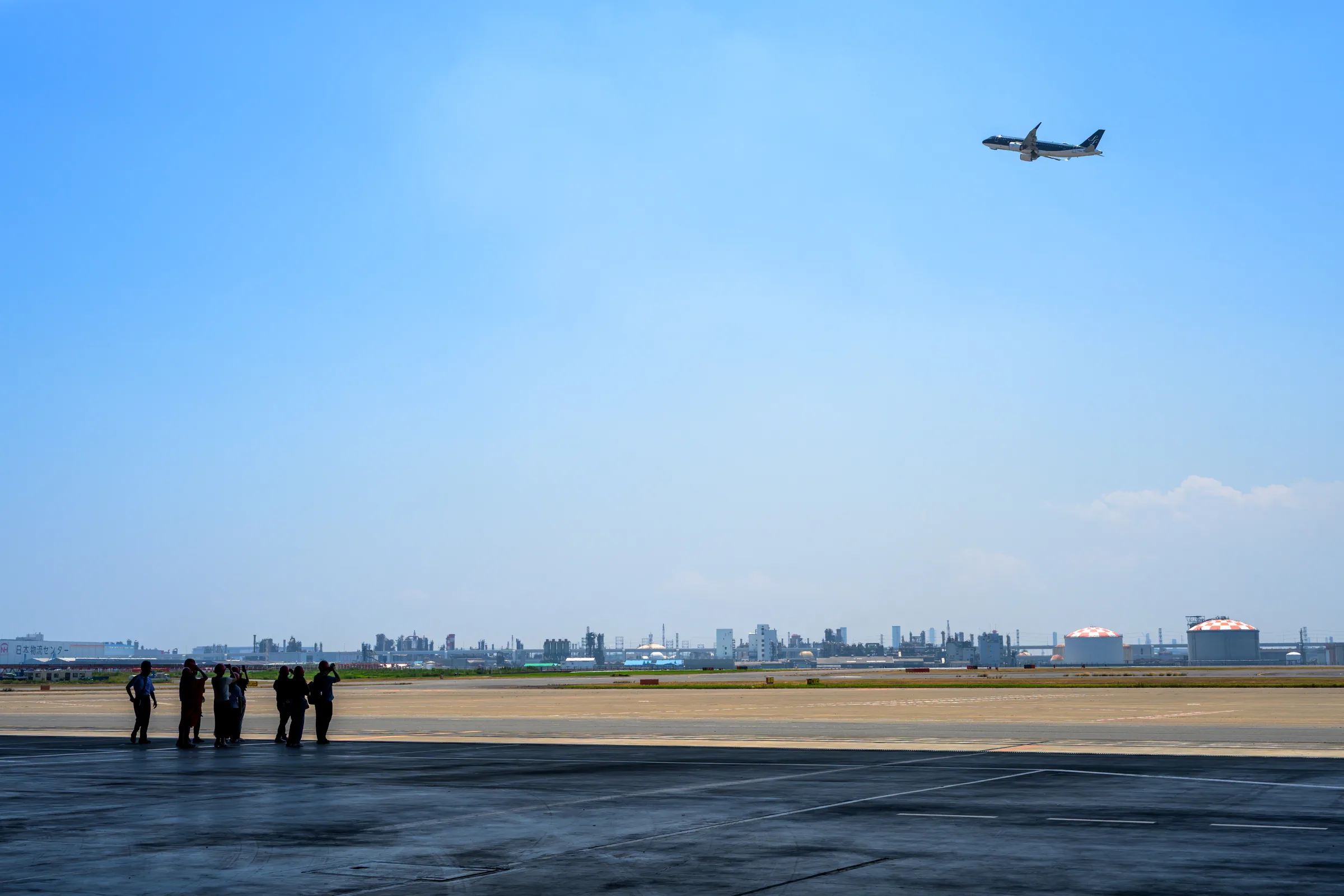 A small group watches an aircraft pass above the open edge of the hangar