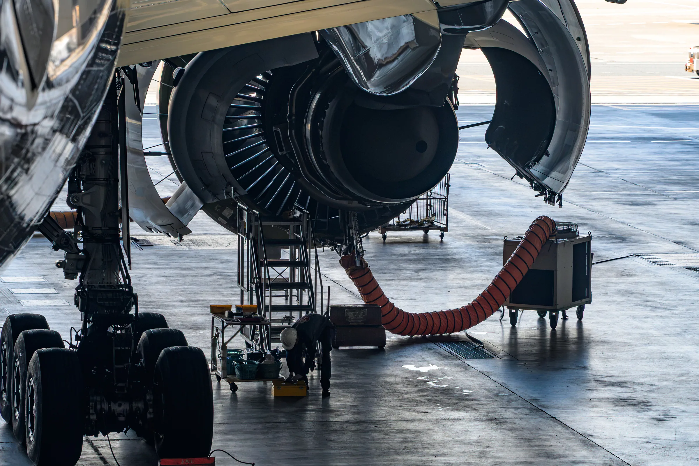 An exposed aircraft engine and service equipment silhouetted inside the hangar