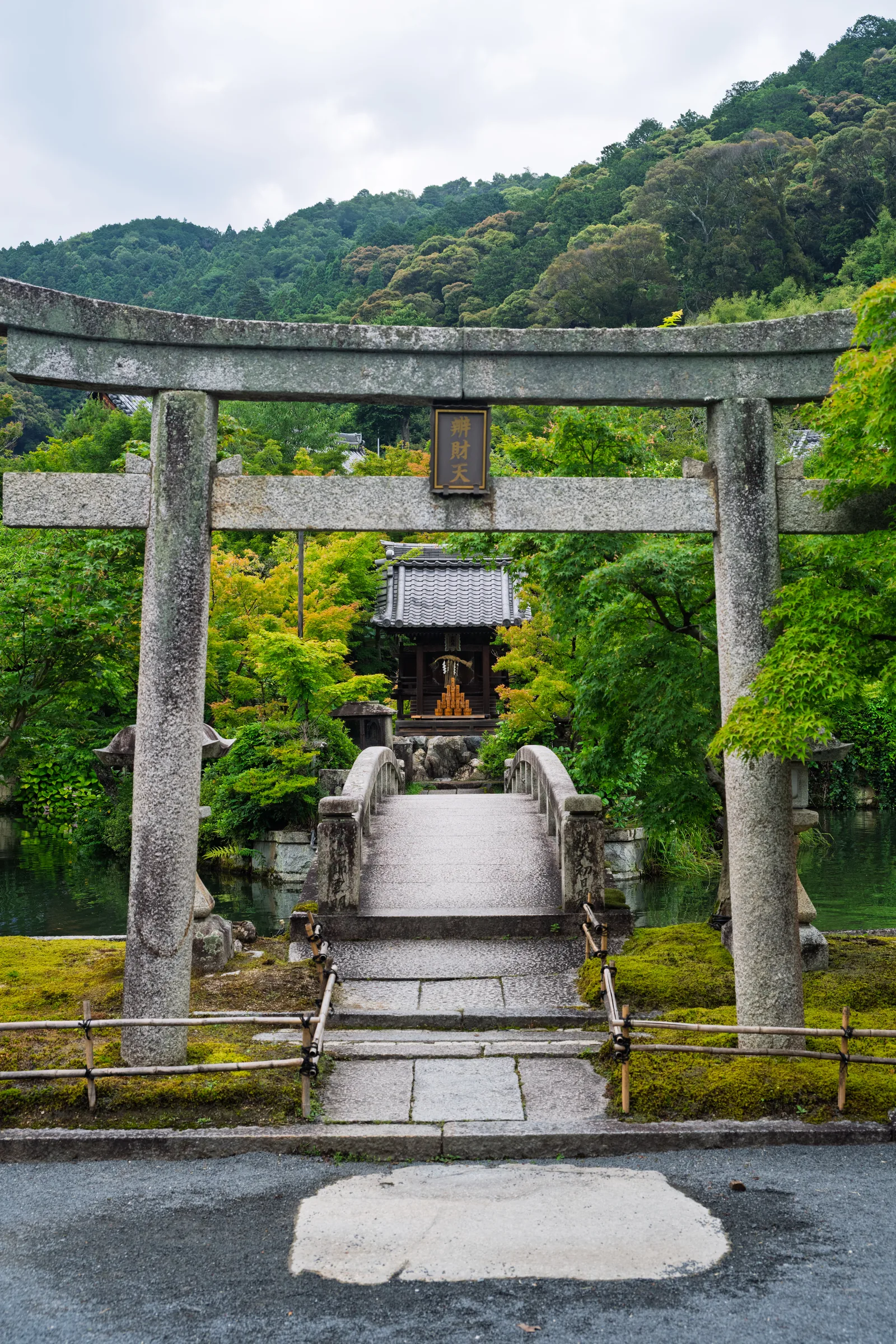 A small stone torii and shrine approached by a narrow path below green hills