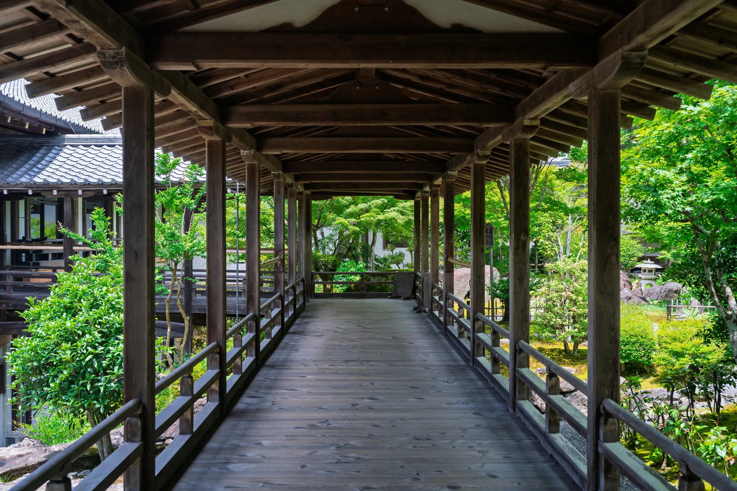 A long covered wooden walkway receding between temple buildings and a garden