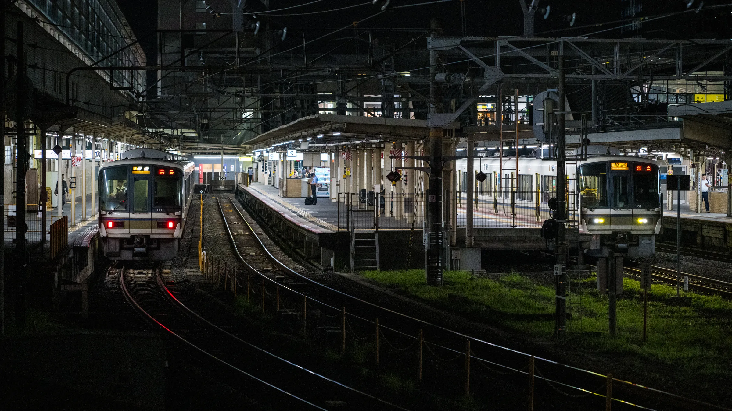 Two commuter trains waiting beneath the industrial roof of Kyoto Station