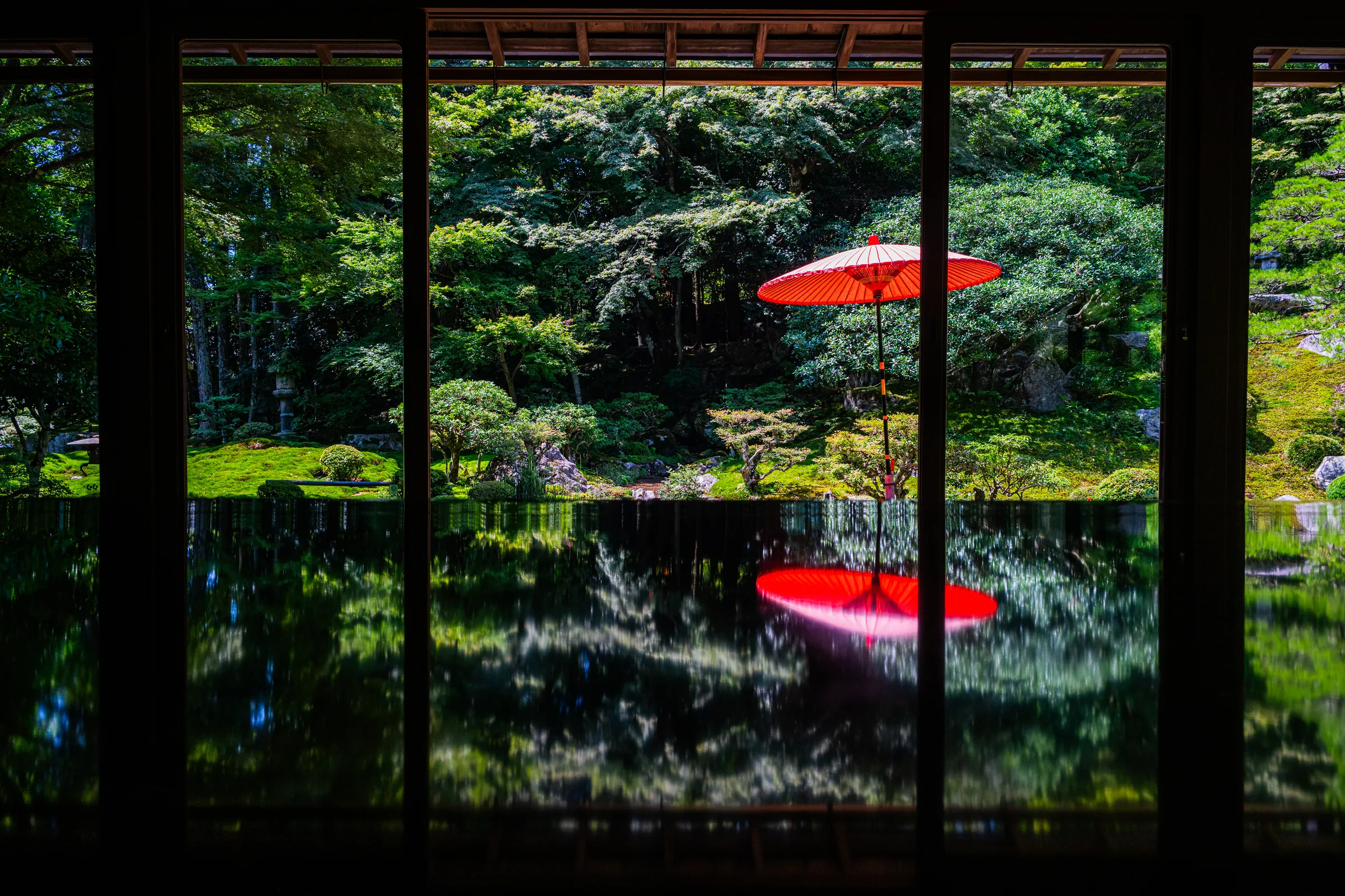 A red parasol and green garden reflected across a black lacquered table