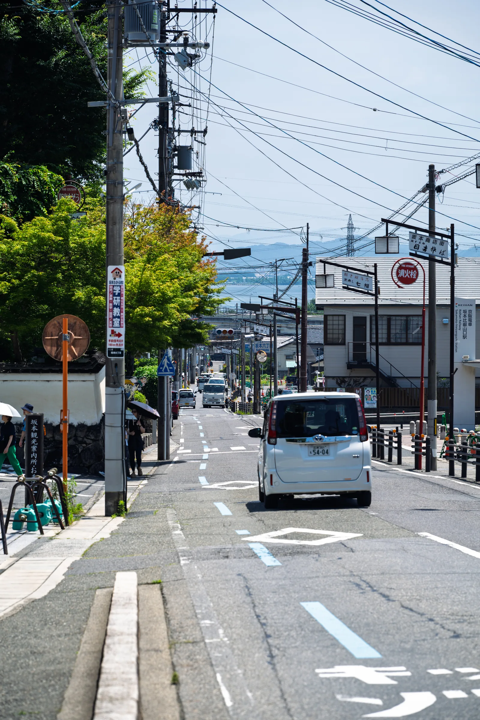 A steep town street descending toward Lake Biwa beneath utility wires