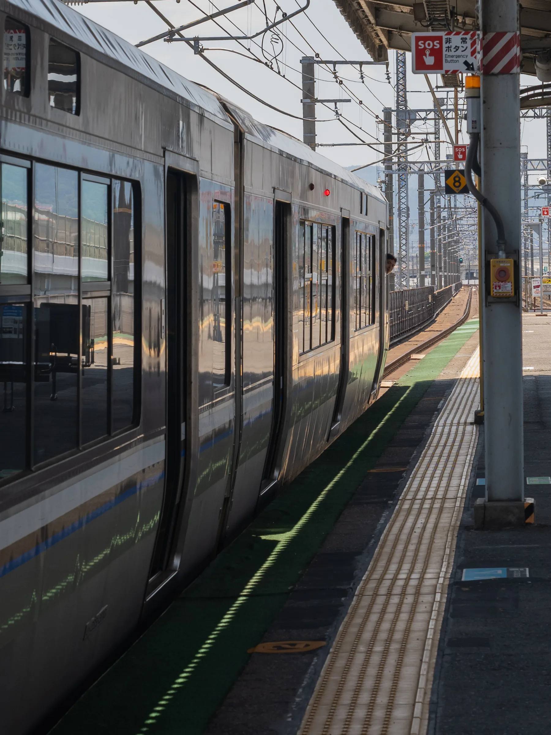 A silver JR commuter train standing beside a sunlit station platform