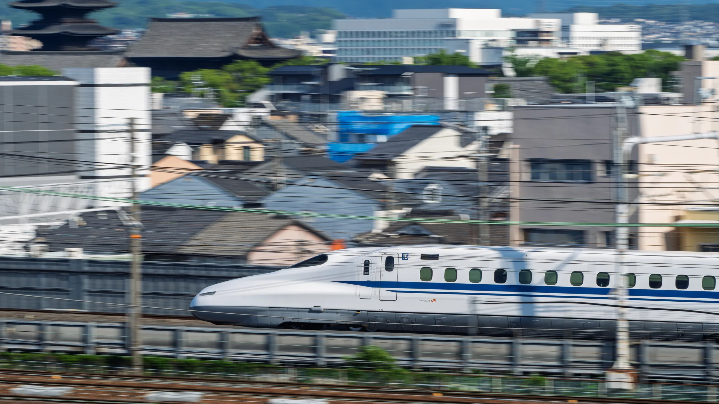 A Shinkansen moving at speed across a layered Kyoto cityscape