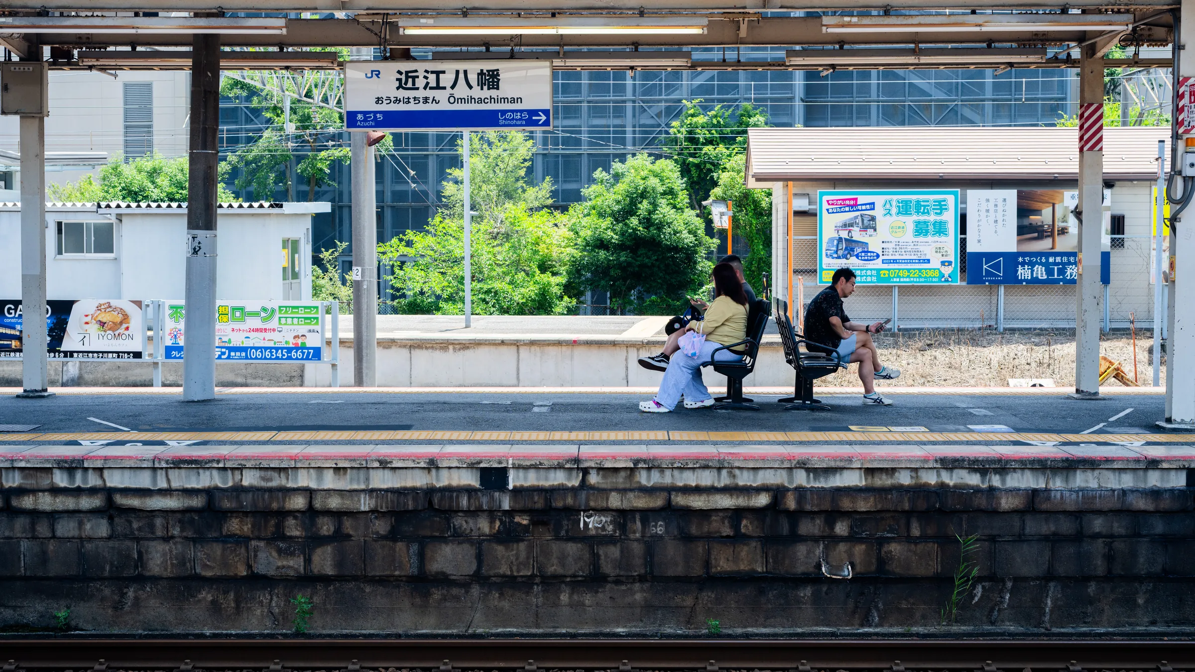 Travelers waiting beneath the Omi-Hachiman station sign on a bright platform