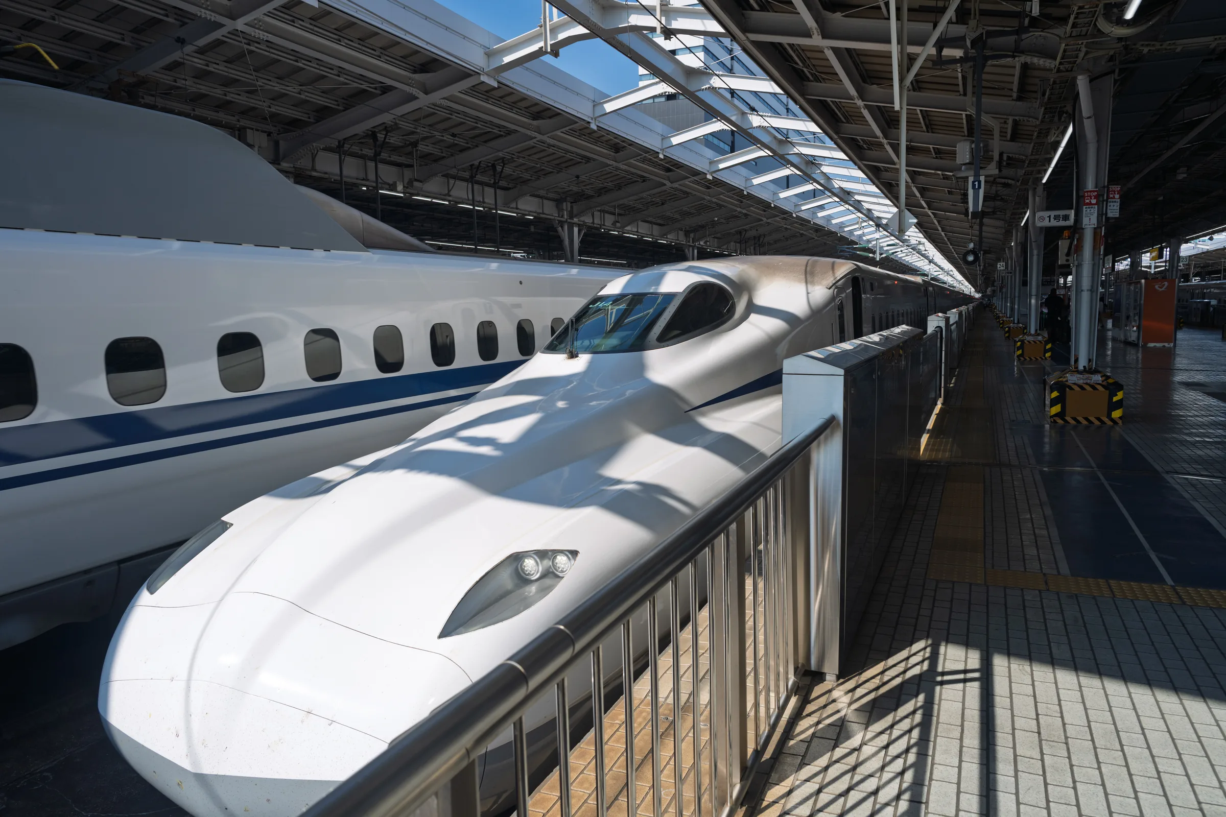 The nose of an N700S Shinkansen patterned by sunlight at a station platform