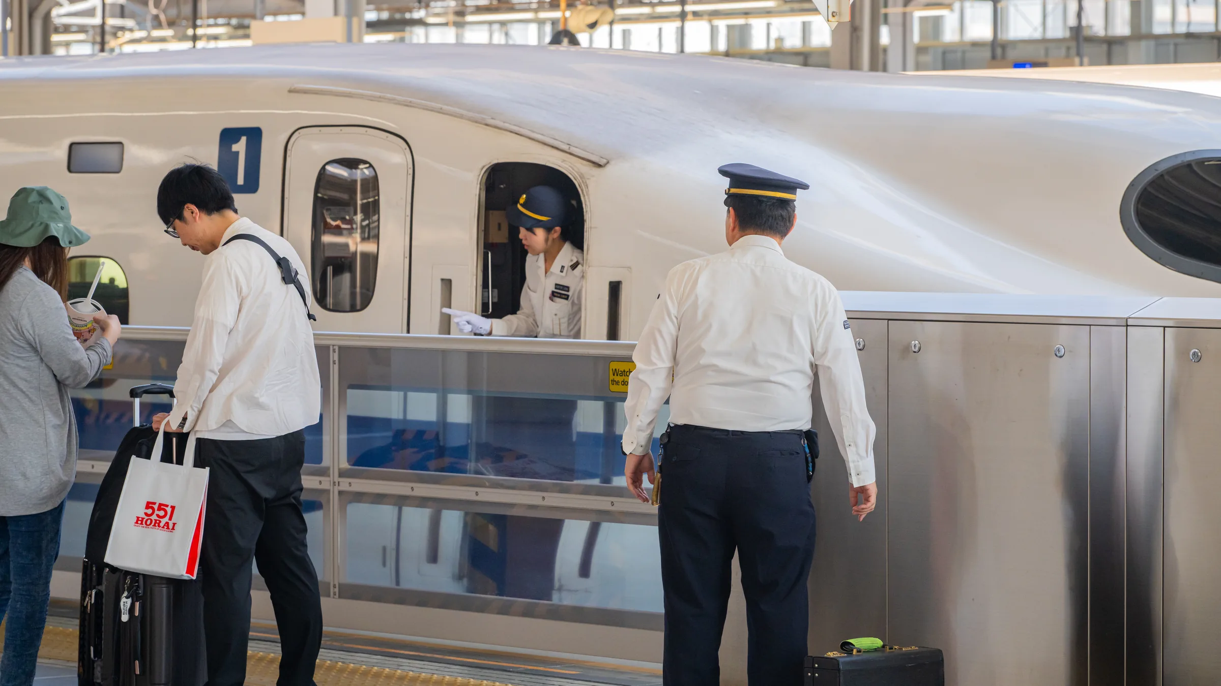 Shinkansen crew coordinating beside an open first-car door as passengers board