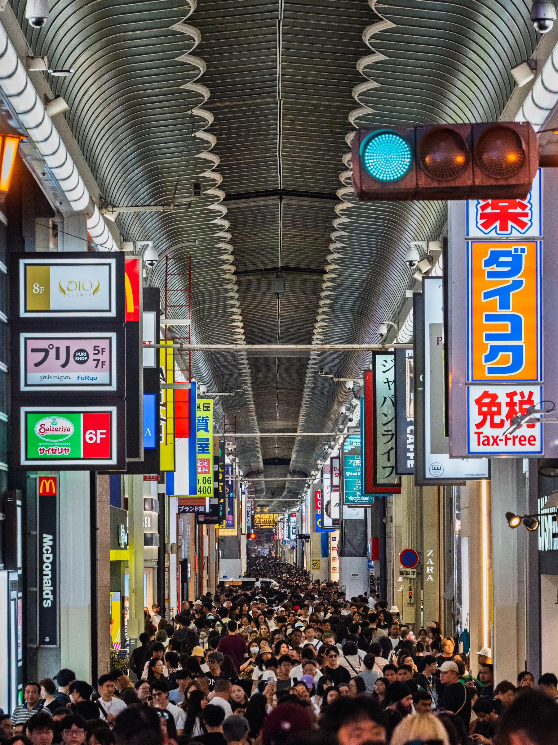 A dense crowd filling a brightly signed covered shopping arcade in Osaka