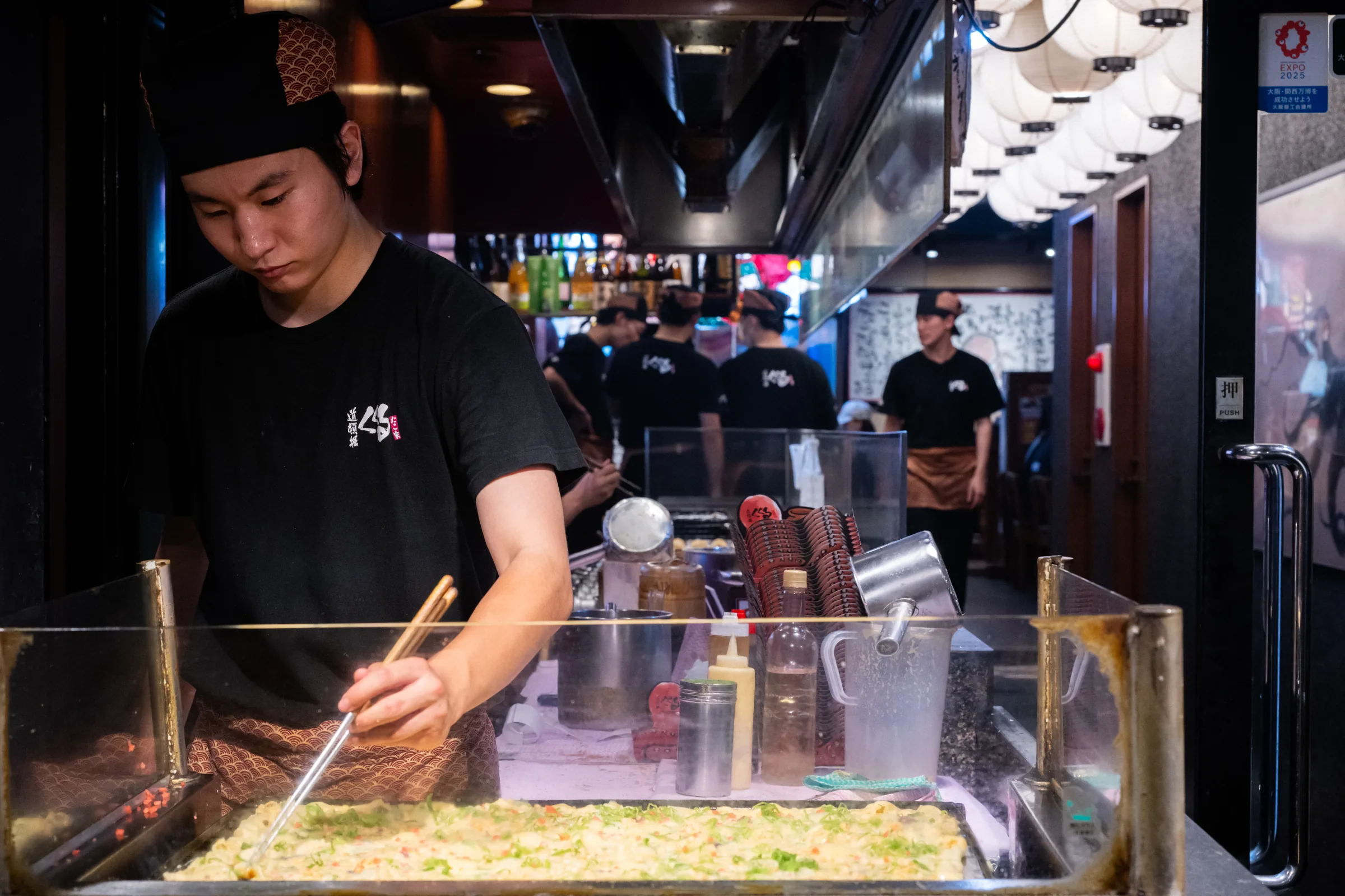 A cook preparing takoyaki behind a bright Osaka shopfront
