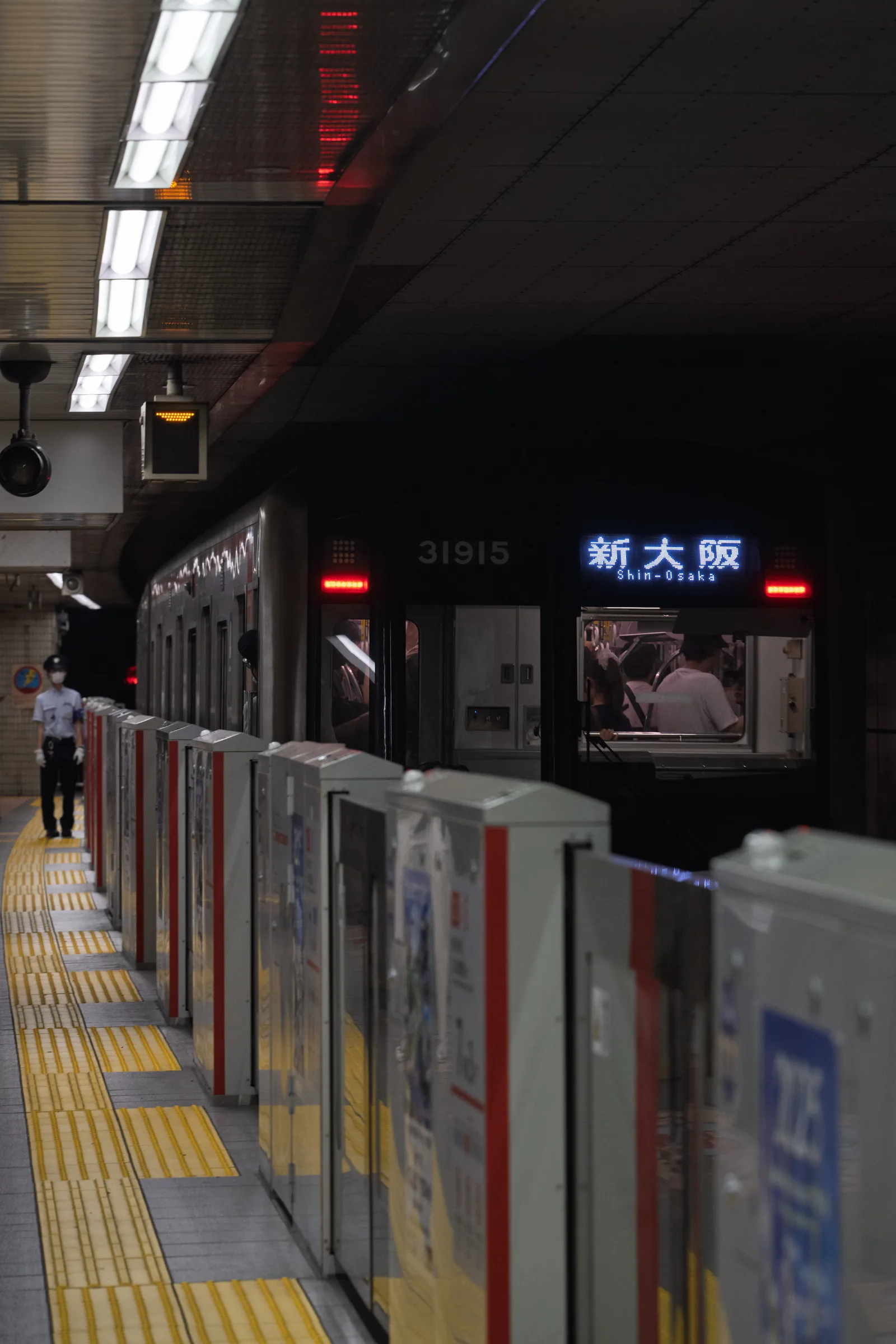 A train waiting behind platform barriers beneath the Shin-Osaka station sign at night