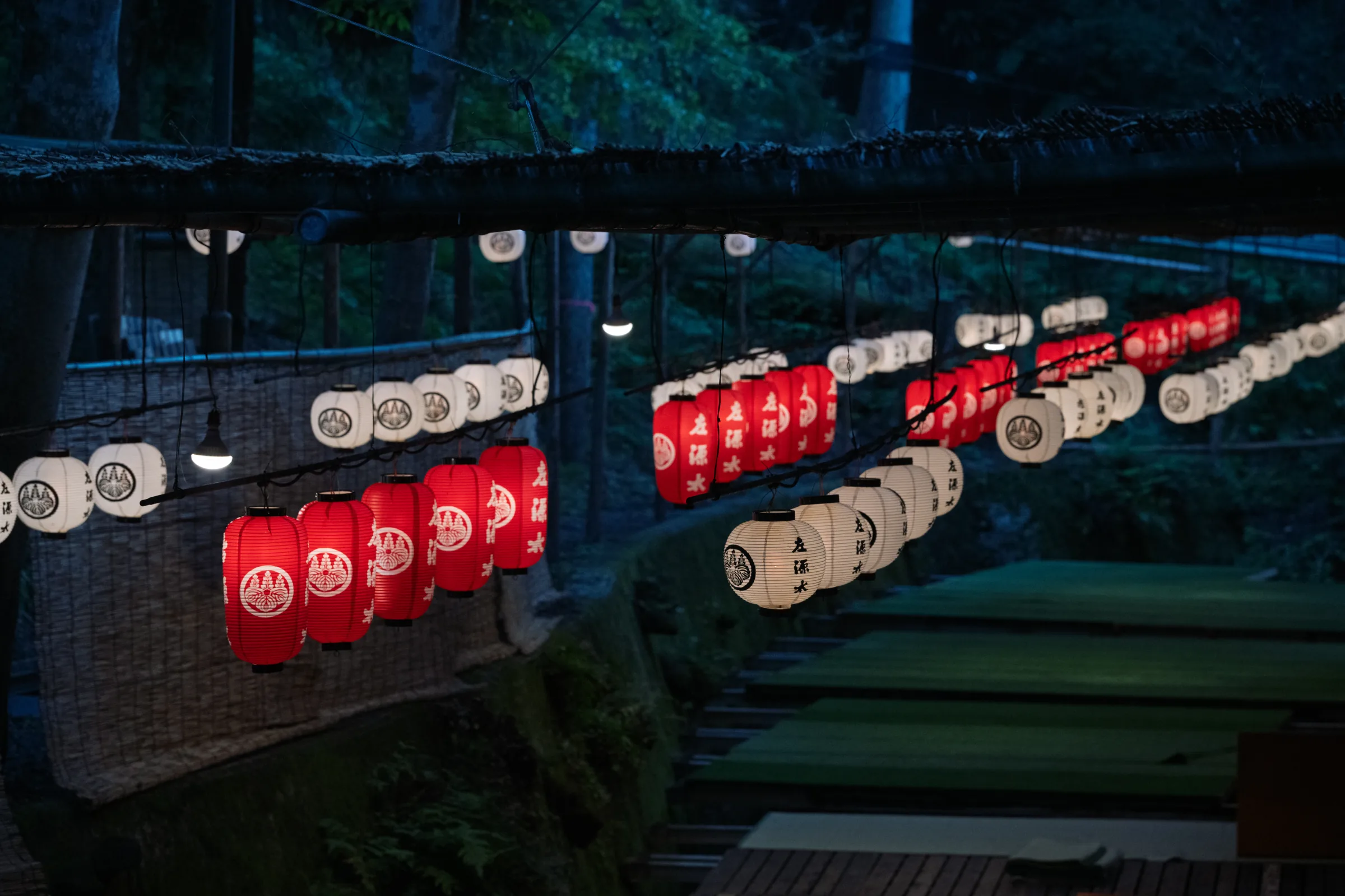 Rows of red and white paper lanterns suspended above a dark summer terrace