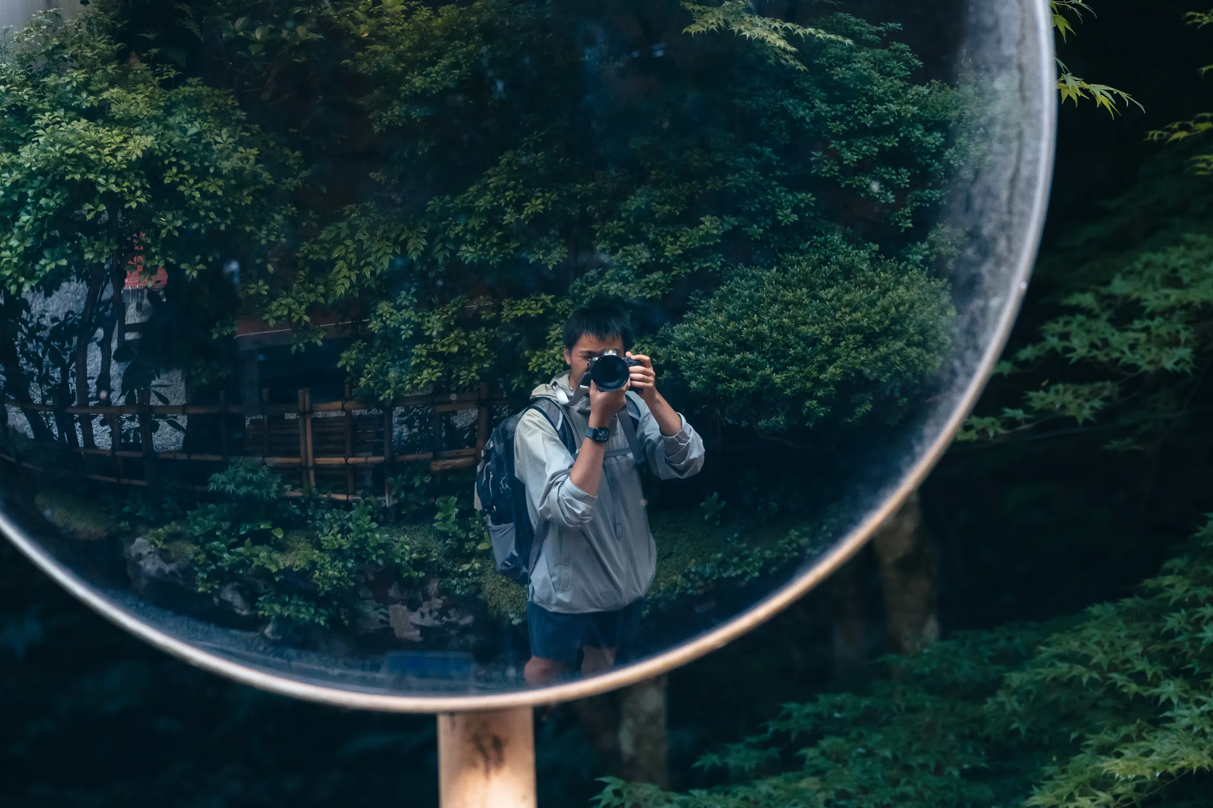 The photographer reflected in a circular roadside mirror surrounded by foliage