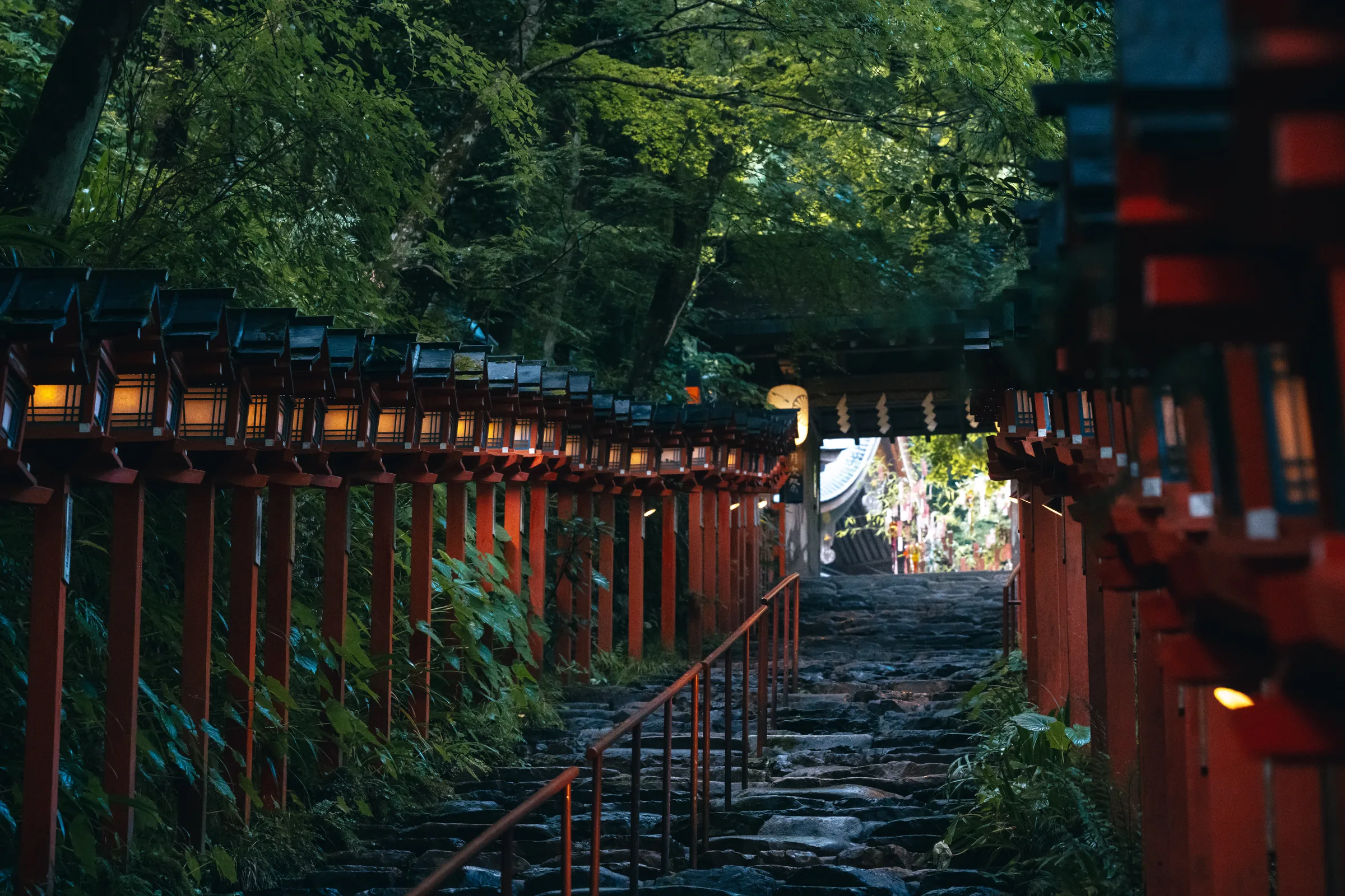 A stone stairway rising between rows of glowing red lanterns at Kifune Shrine