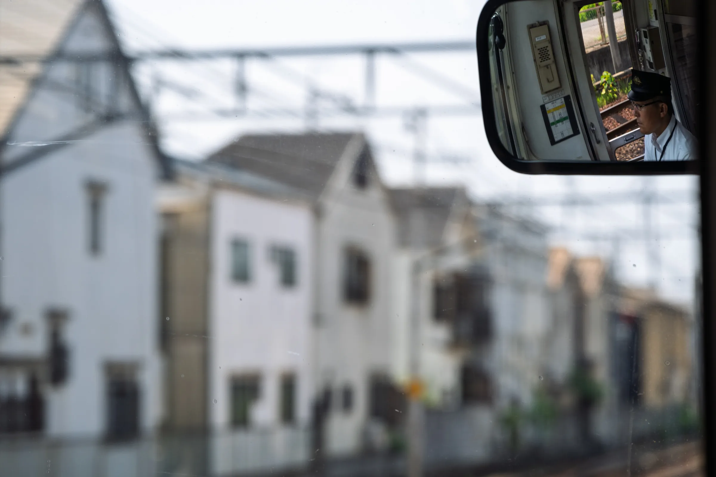 A convex train mirror holding the driver's reflection above blurred houses
