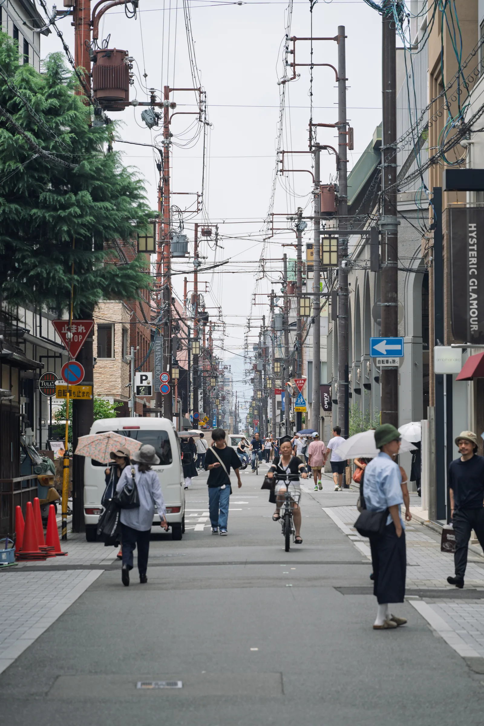Pedestrians moving along a narrow commercial street beneath utility wires