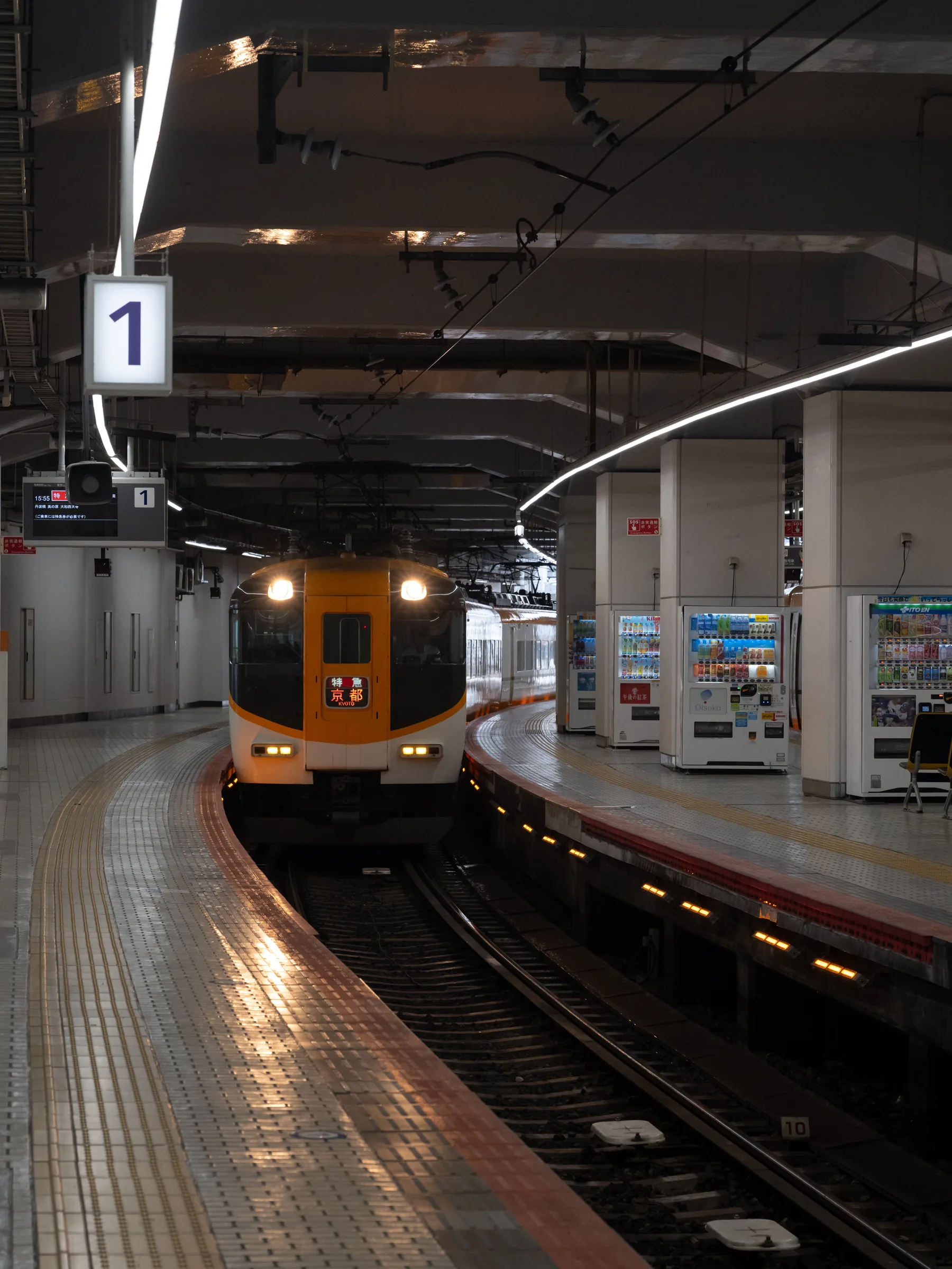 An orange Kintetsu limited express waiting beneath the number one platform sign
