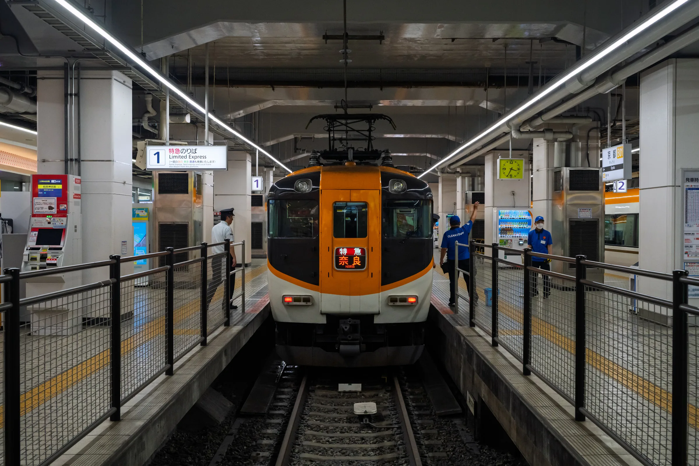 An orange Kintetsu train seen head-on between platform fences