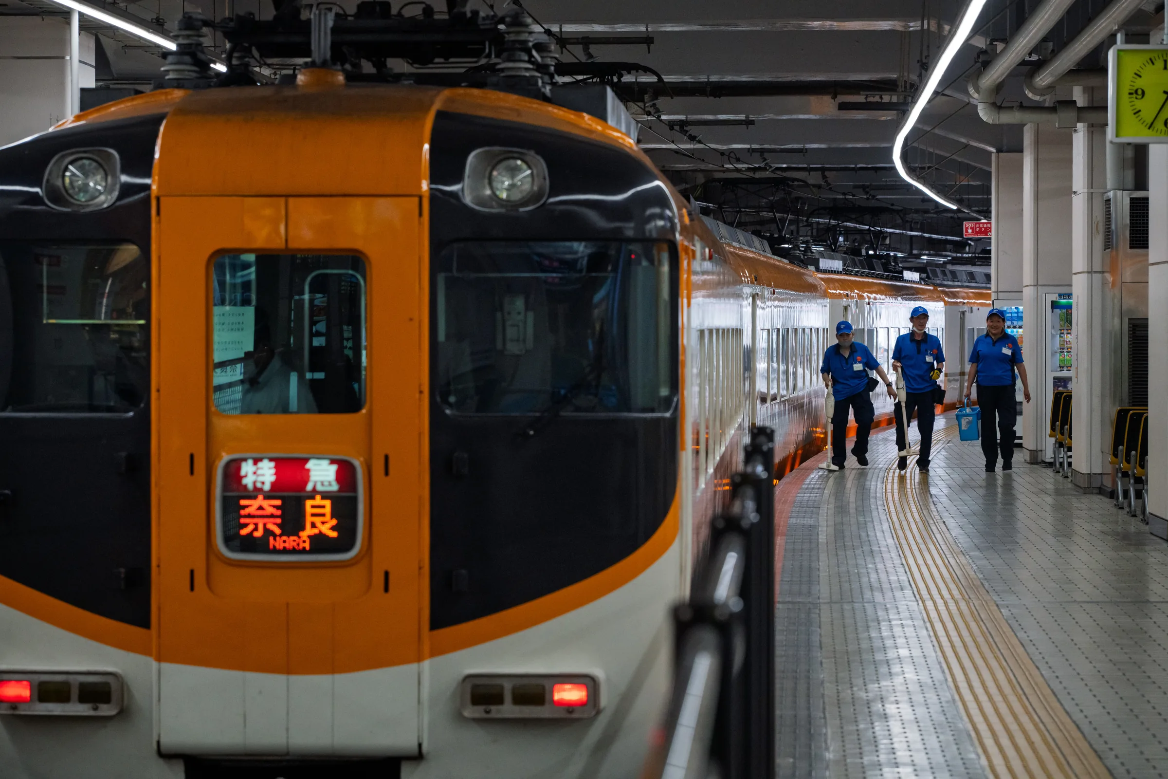 An orange Kintetsu limited express for Nara beside three railway workers
