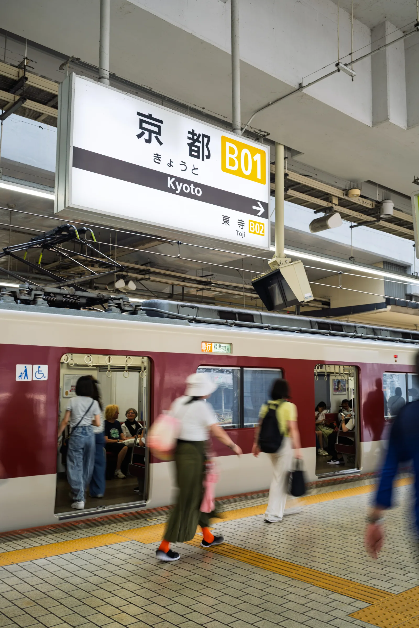 A red Kintetsu train standing beneath the Kyoto Station platform sign
