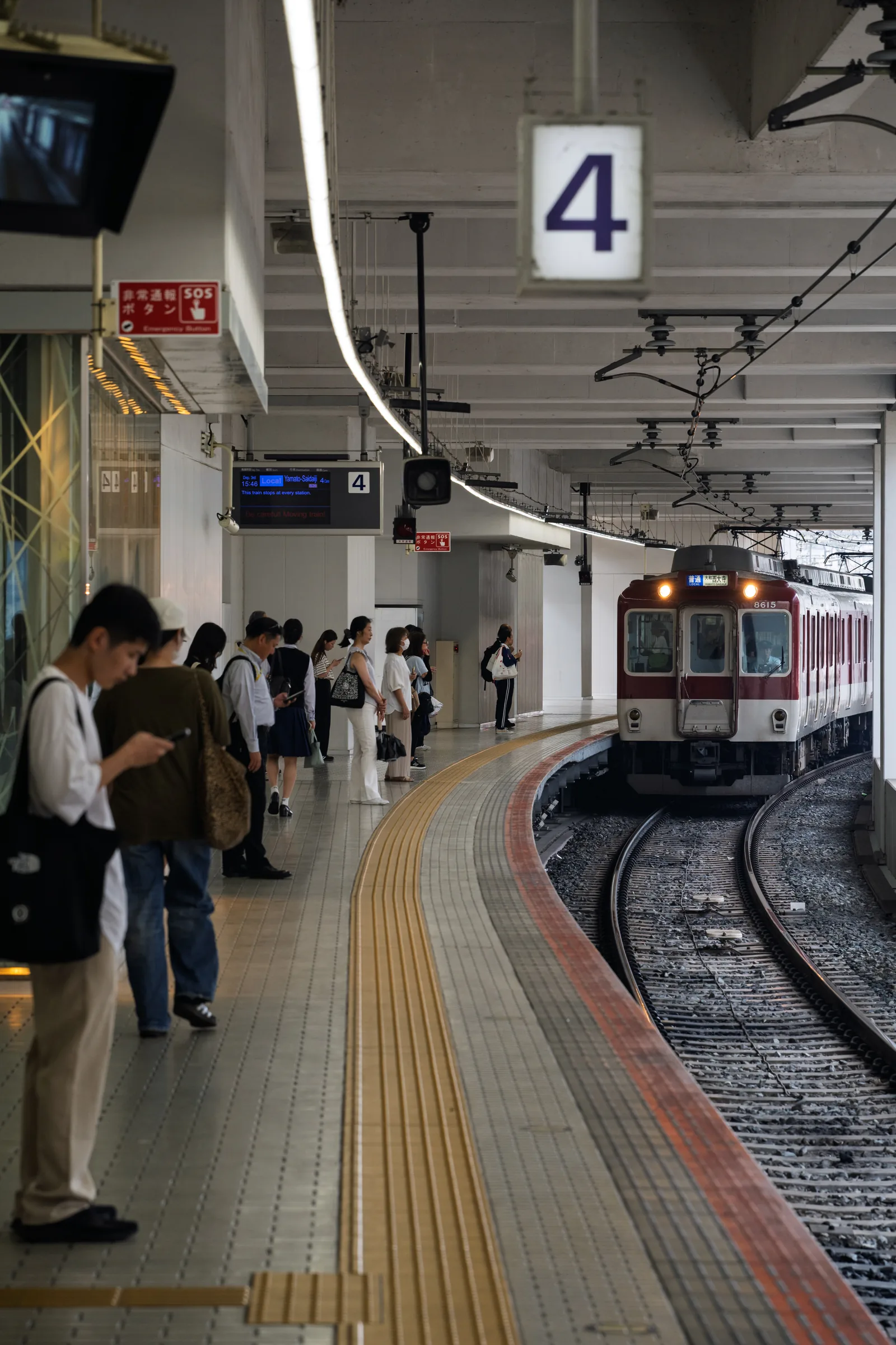 A Kintetsu train curving into platform four beside waiting passengers
