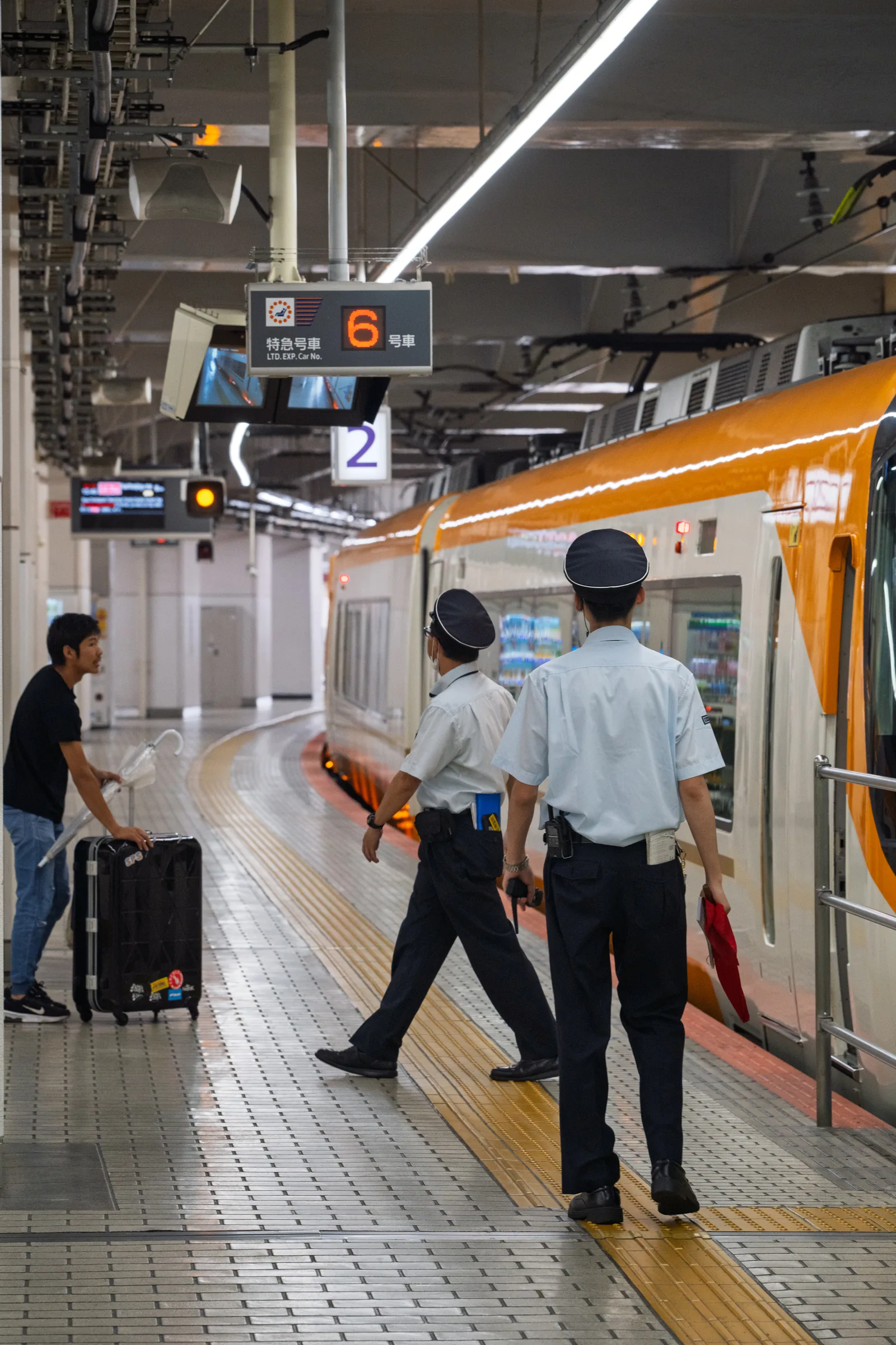 Railway staff walking across a platform beside an orange limited express