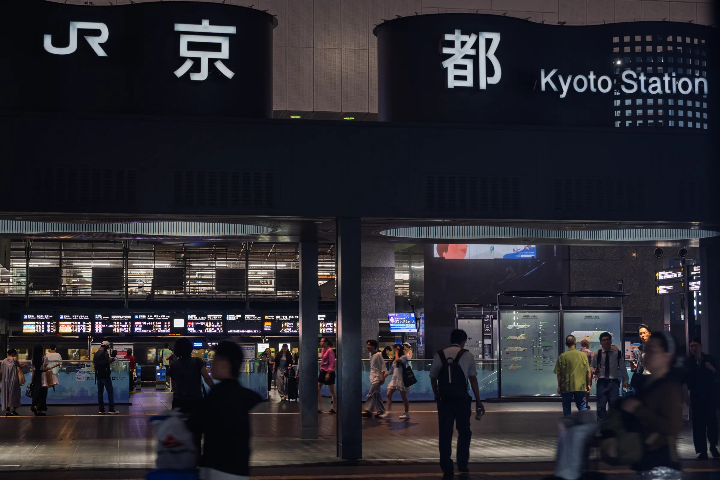 Travelers standing beneath the illuminated Kyoto Station sign at night