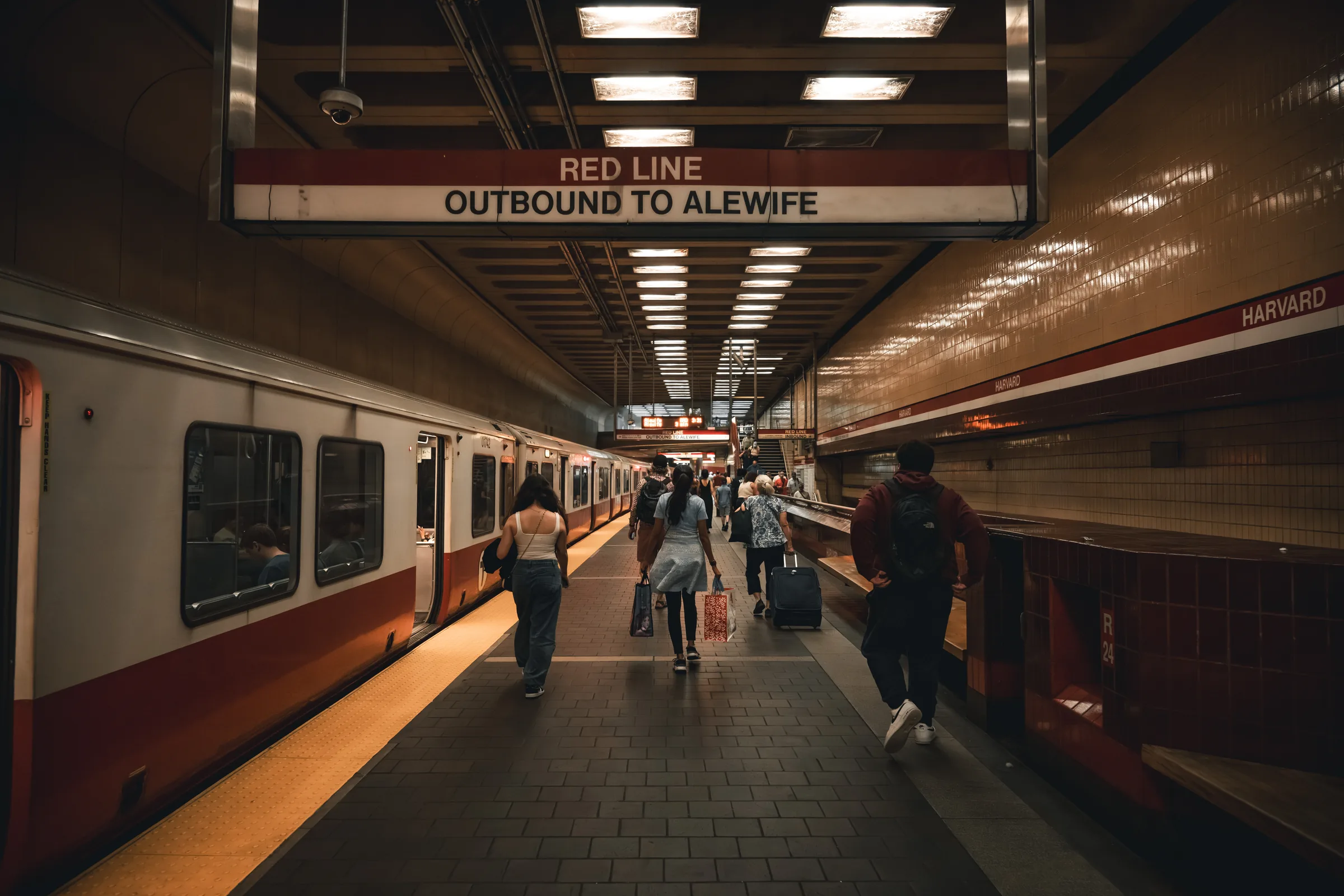 Commuters walking along Harvard station beside a Red Line train bound for Alewife