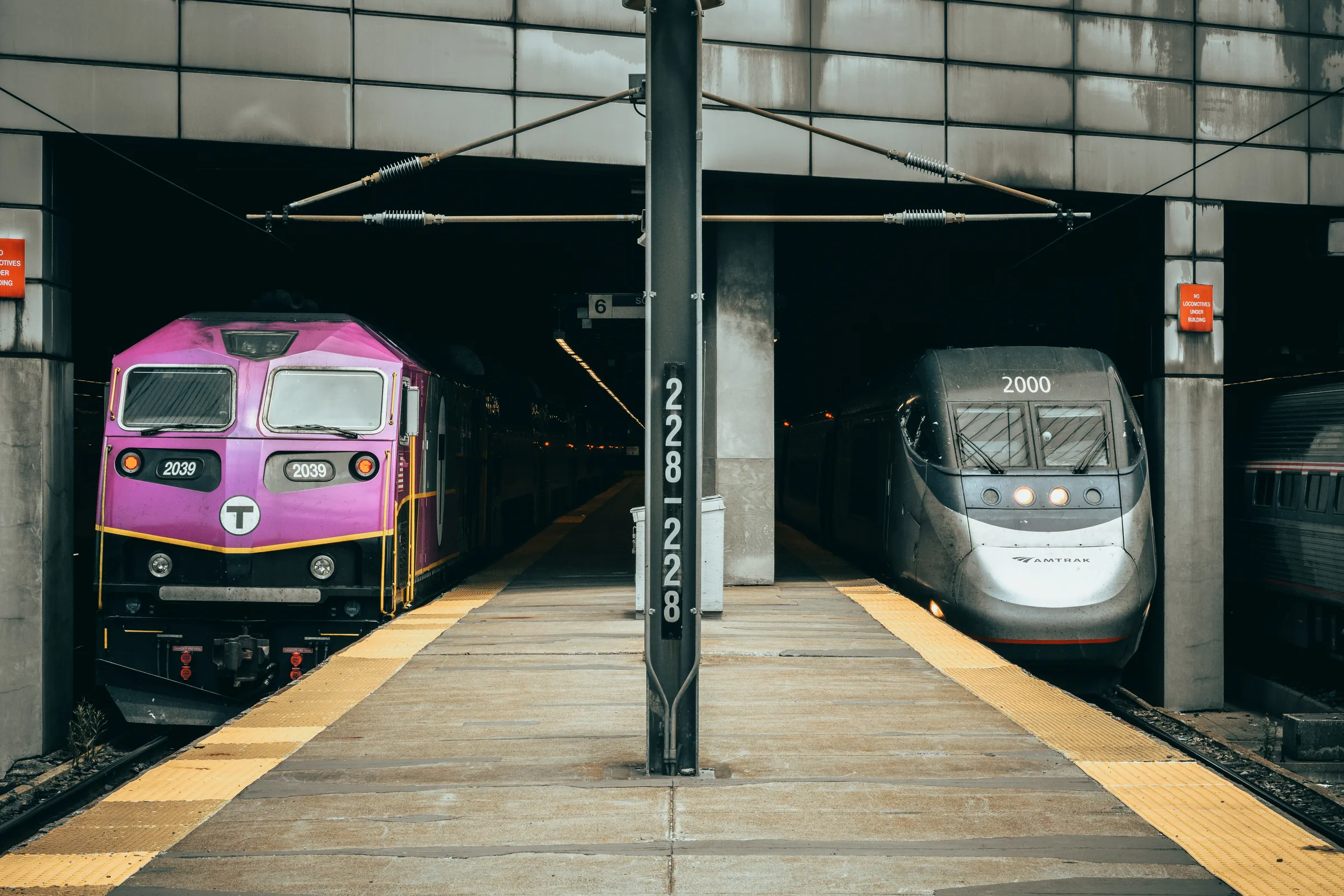 A purple commuter locomotive and a silver intercity train waiting side by side at a terminal