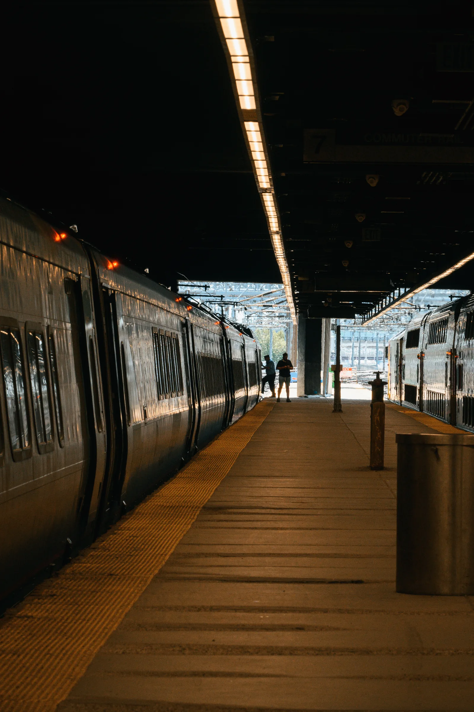 A nearly empty commuter-rail platform stretching from a dark canopy toward daylight