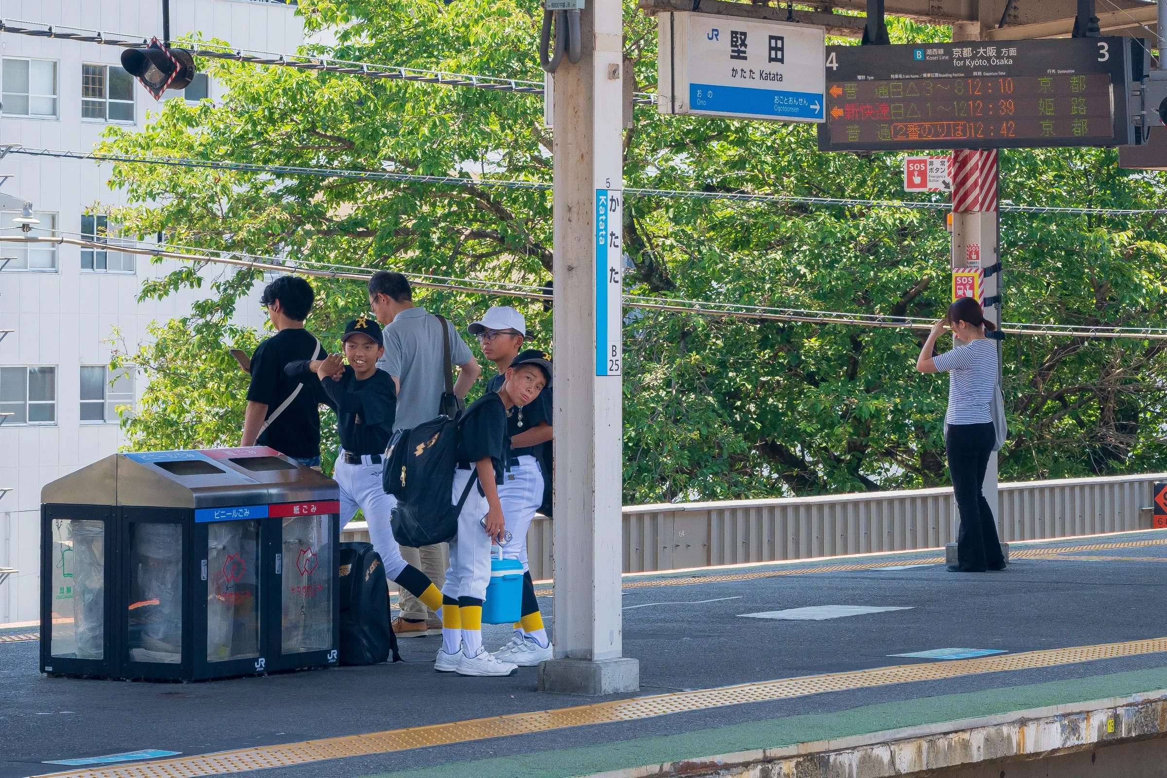 Young baseball players in uniform waiting with their bags on a sunny station platform