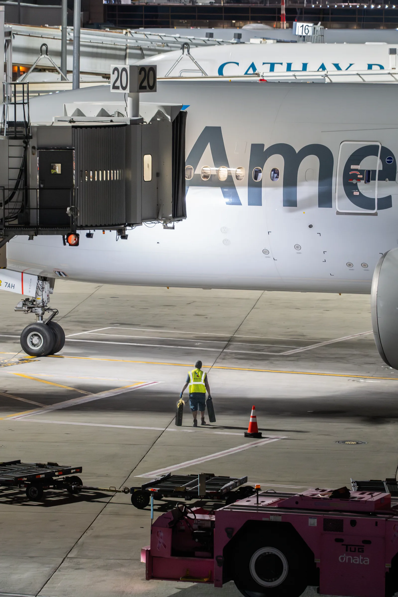 A ground crew member standing alone beneath an American Airlines aircraft beside a pushback tug