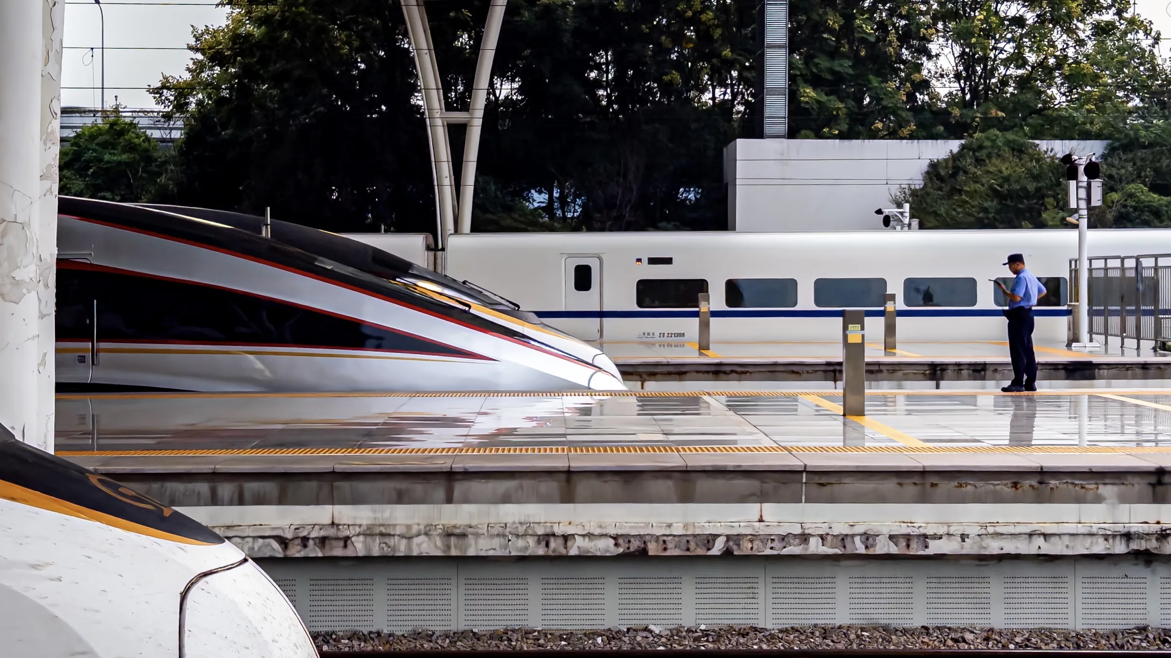 A high-speed train blurring past a platform worker standing between two tracks
